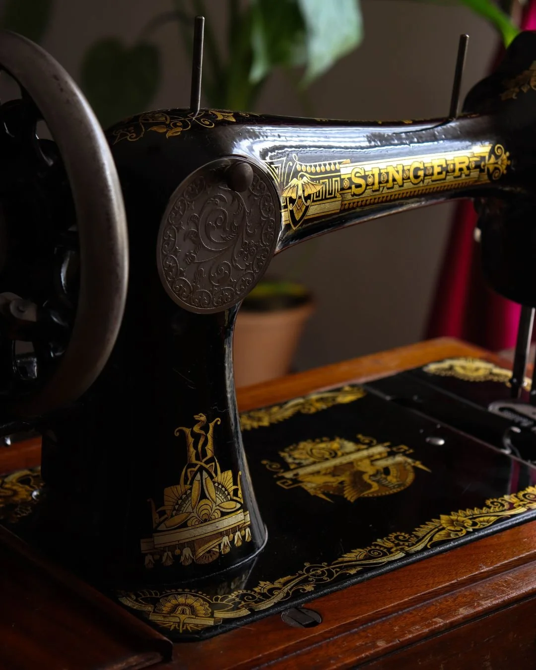 Machine à coudre vintage noire avec des ornements et le nom 'SINGER' en or, posée sur une table en bois.