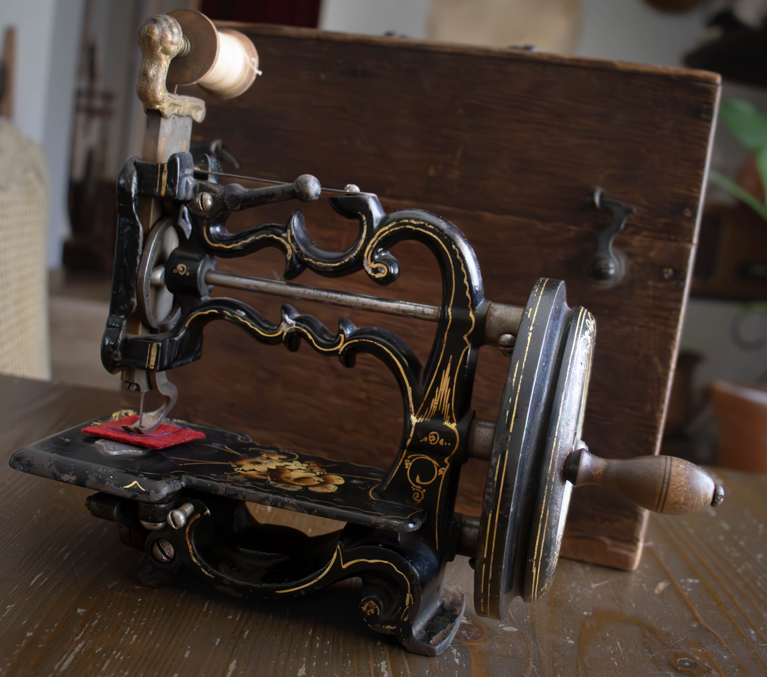 Une machine à coudre ancienne en métal noir avec des détails dorés, posée sur une table en bois sombre, avec un bobine de fil blanc sur le support.