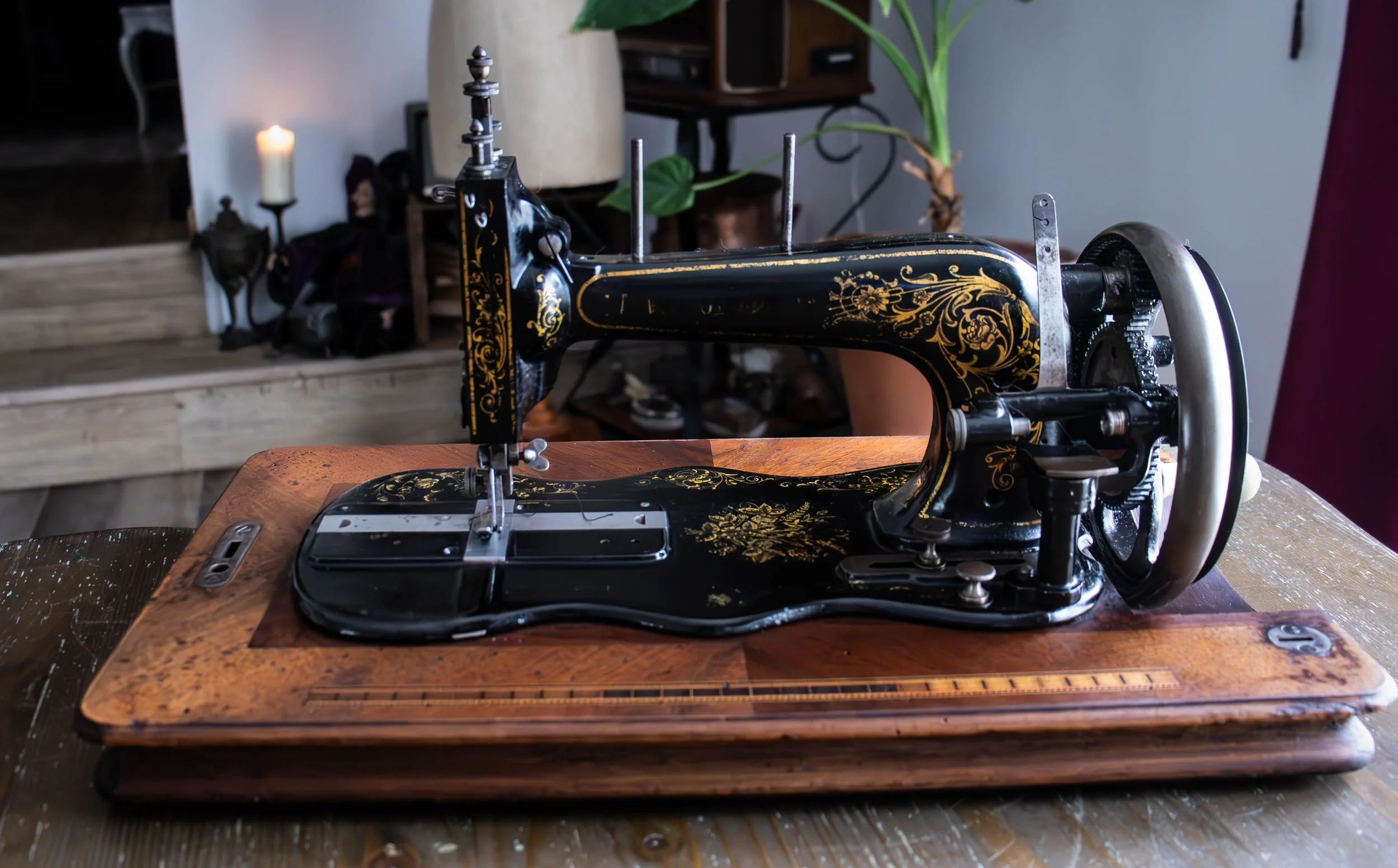 Une machine à coudre vintage noire avec des motifs dorés, placée sur une table en bois.