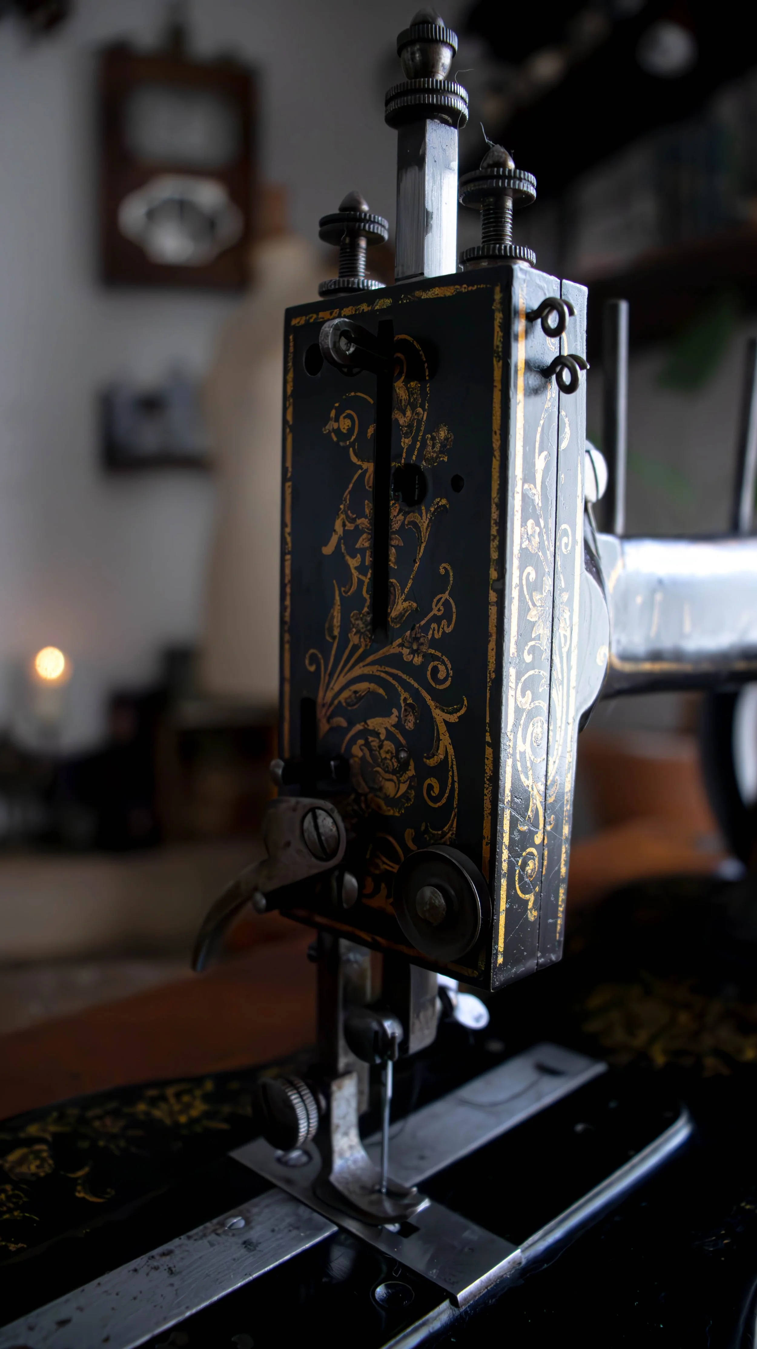 Une machine à coudre ancienne avec un motif floral doré sur un fond noir, en intérieur, avec un décor flou en arrière-plan.
