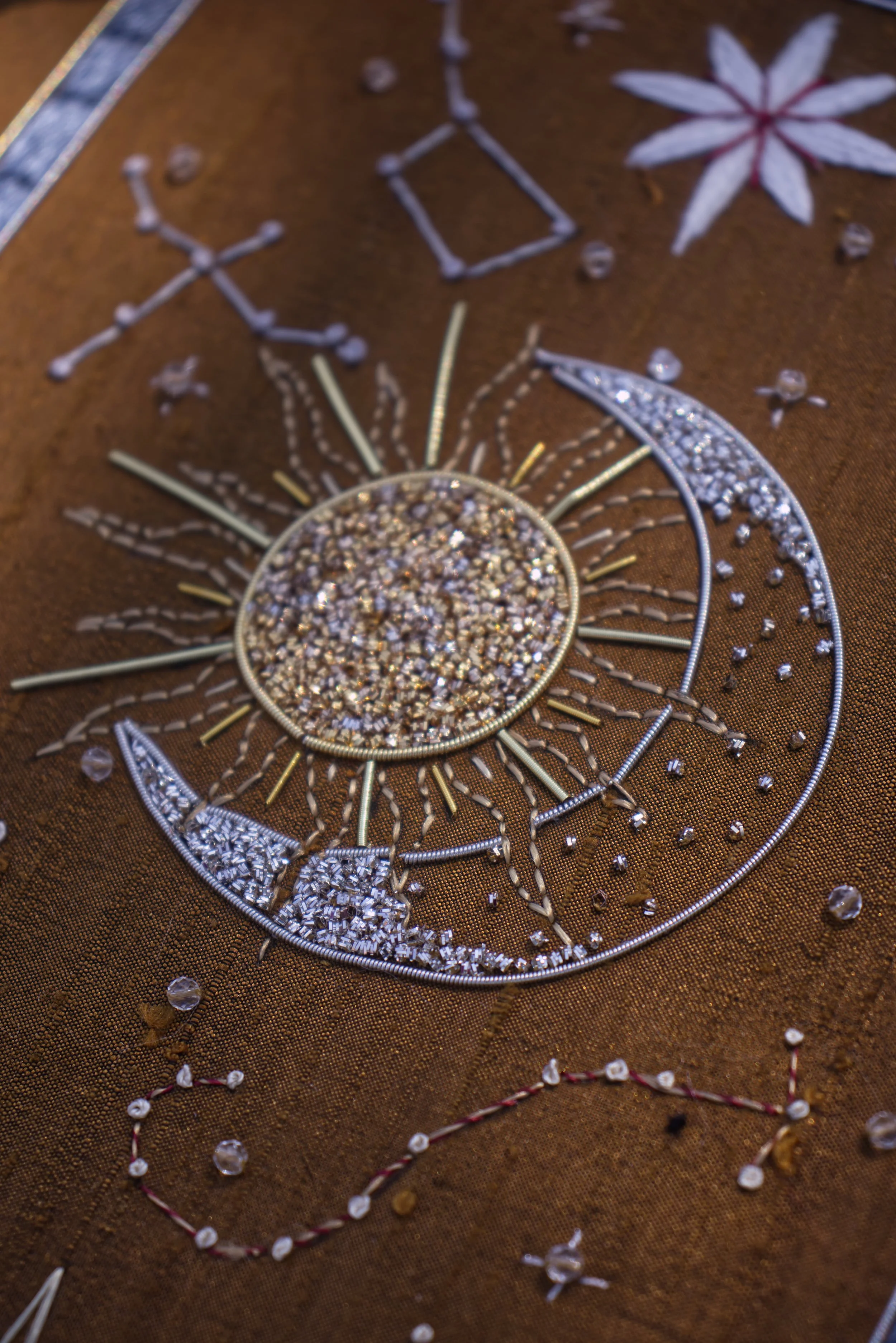 Une pièce d'artisanat en métal et perles, représentant un soleil avec un visage, décoré de motifs floraux et géométriques, posée sur un tissu brun foncé.