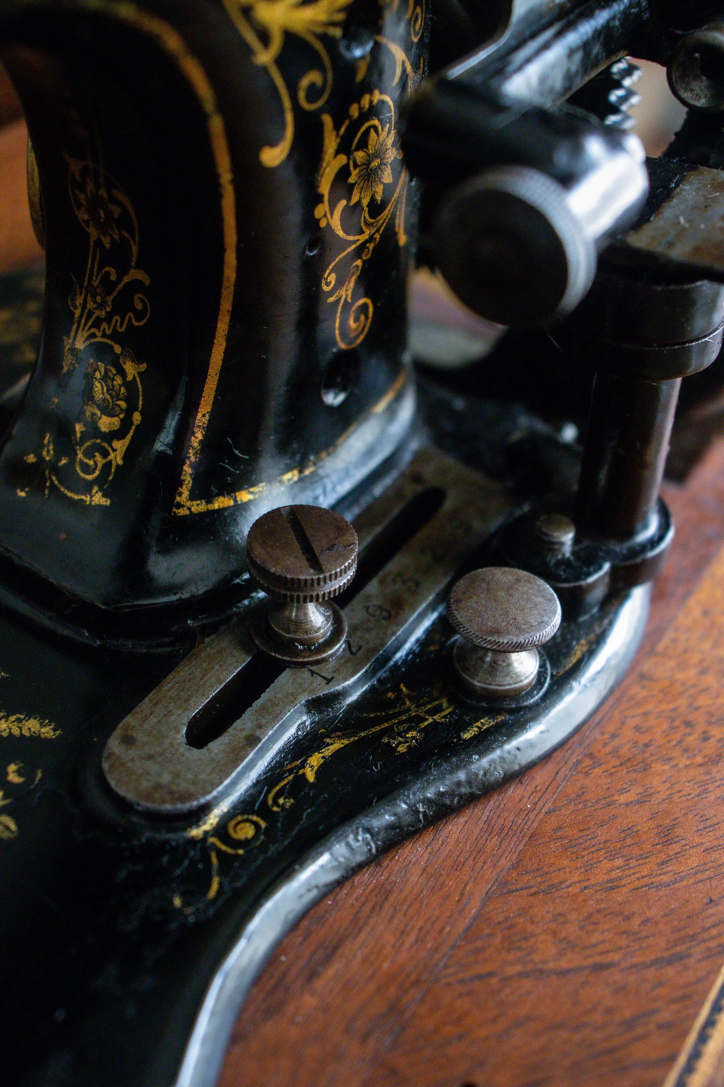 Détail d'une machine à coudre ancienne avec des décorations en or noir et des boutons en métal.