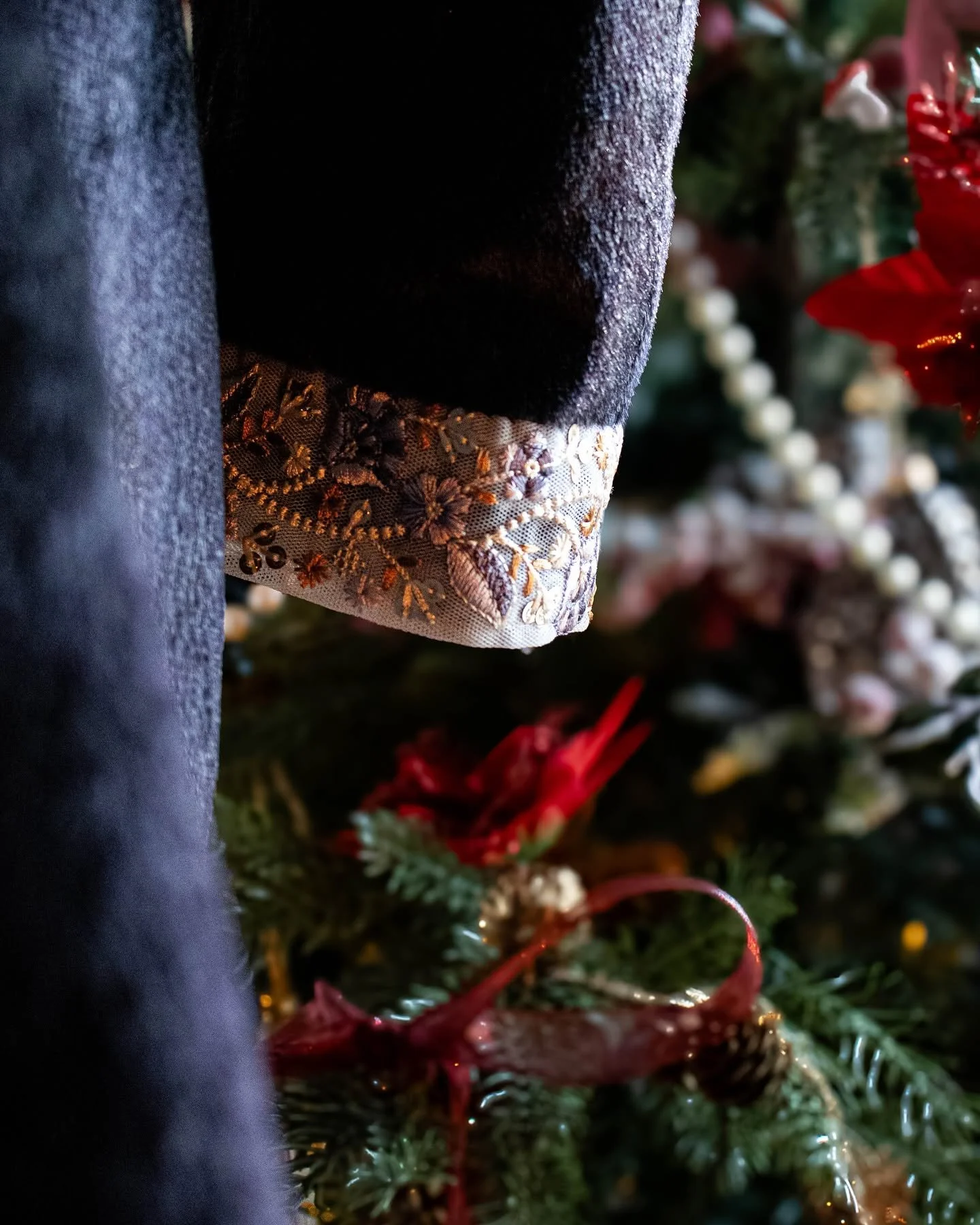 partie d'une décoration de Noël avec un sapin, un tissu noir avec broderie florale et une personne portant un vêtement en denim