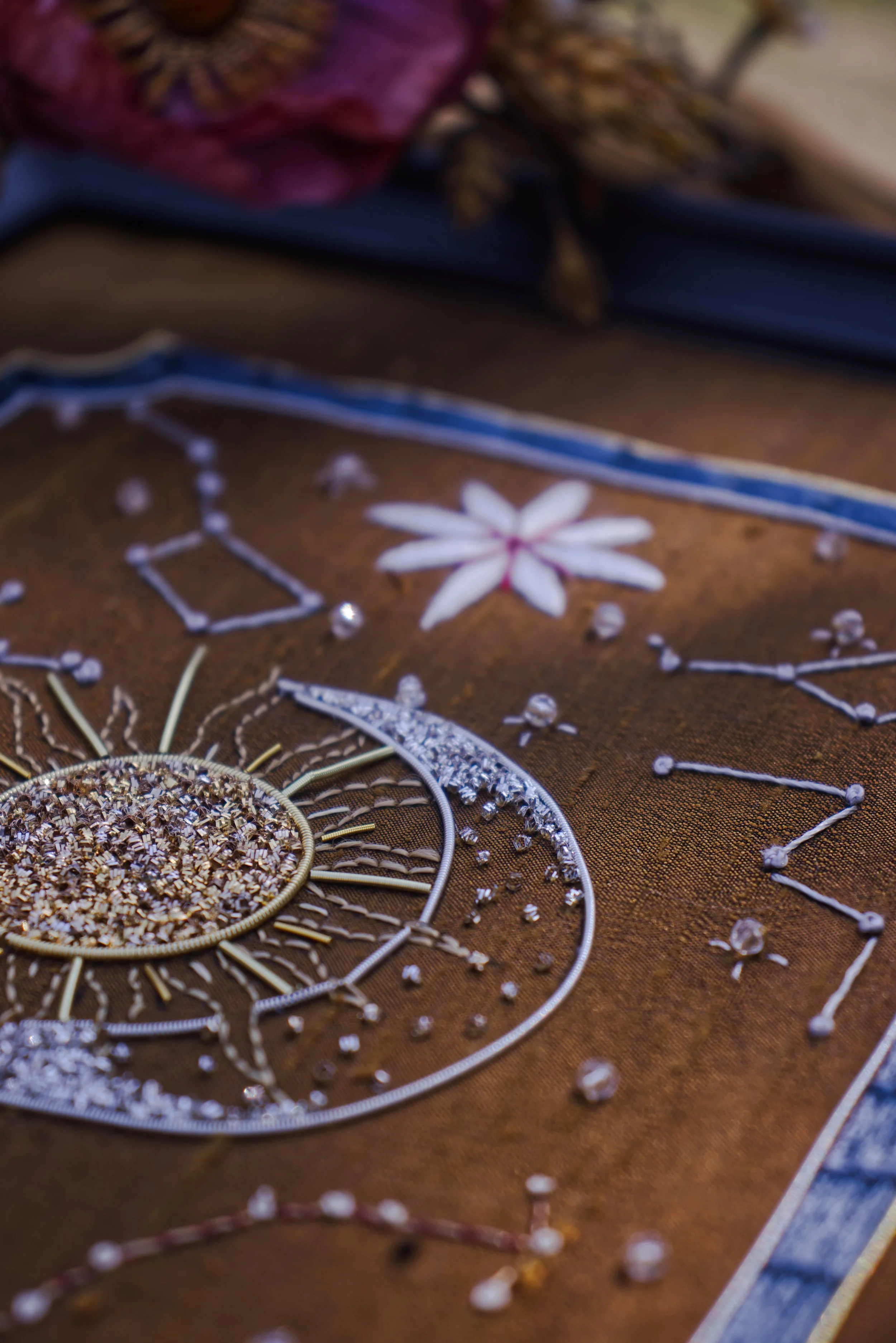 Décoration en fil métallique avec perles, fleurs en tissu, et éléments de broderie, sur une surface en tissu marron.