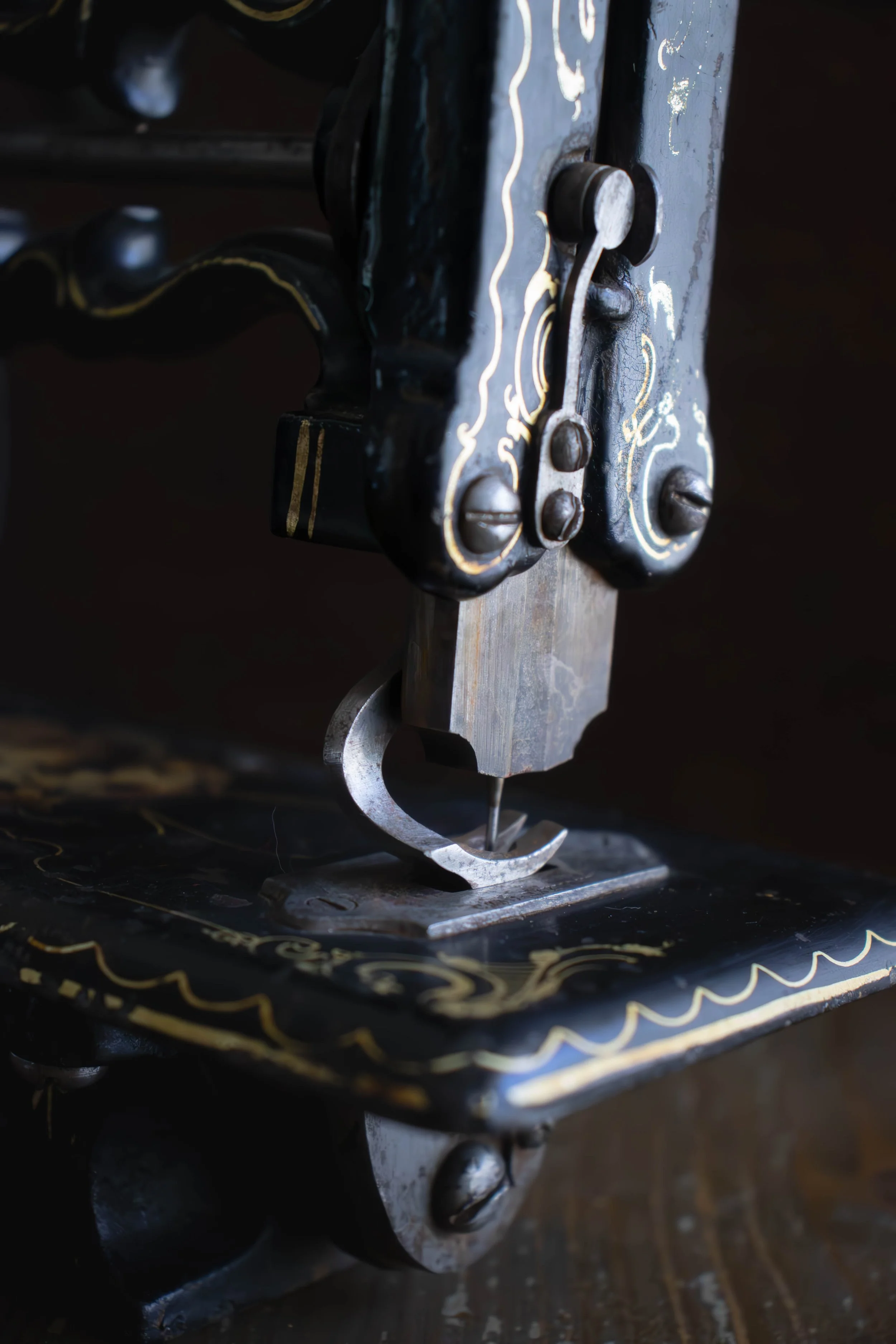 Une vieille machine à coudre en métal noire avec des détails dorés et un bras en métal, fixée sur une surface en bois