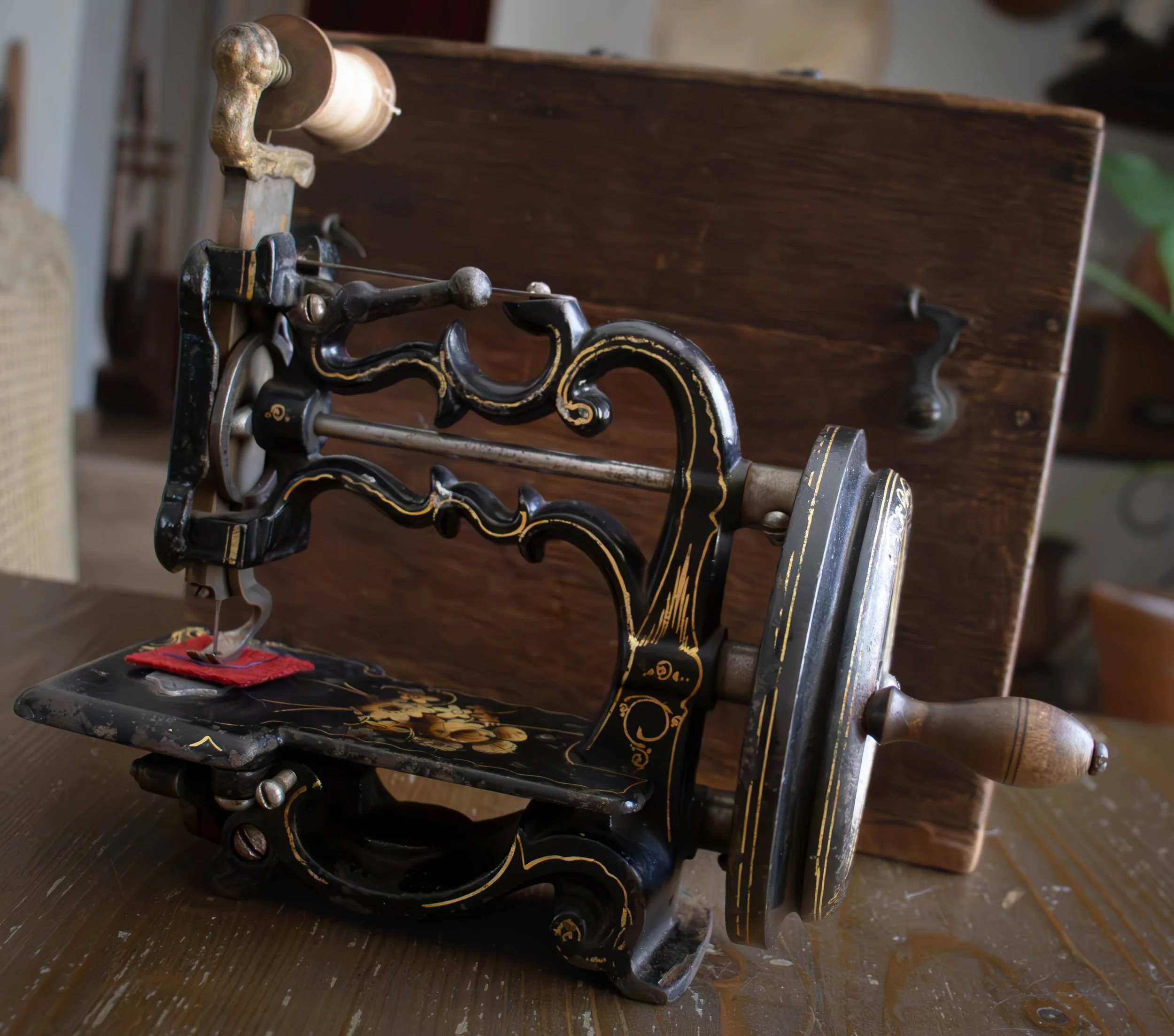 Une vieille machine à coudre en métal noir avec des ornements dorés, posée sur une surface en bois, avec une bobine de fil sur le dessus.