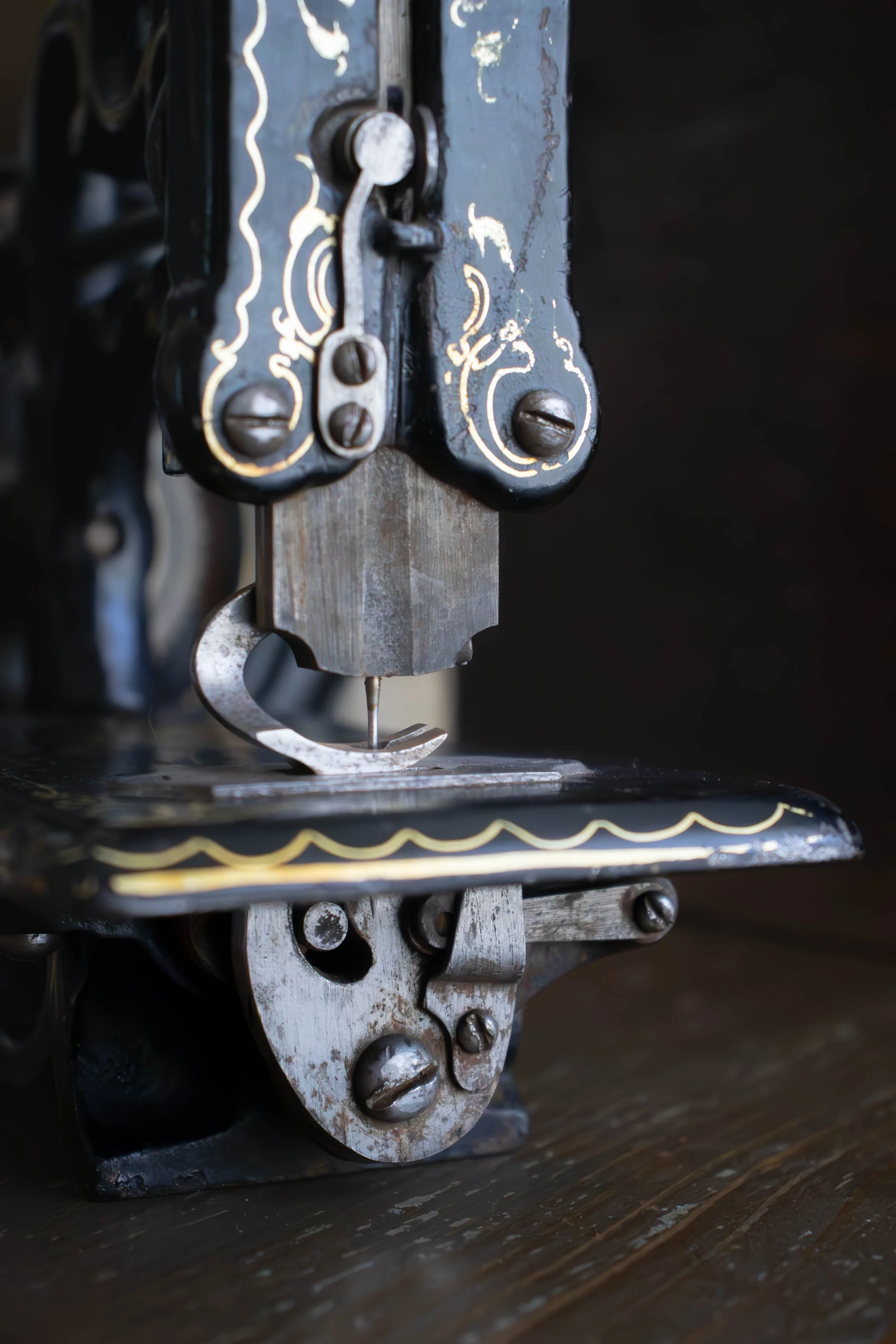 Détails d'une machine à coudre ancienne en acier, avec des vis et des décorations dorées, posée sur une surface en bois.