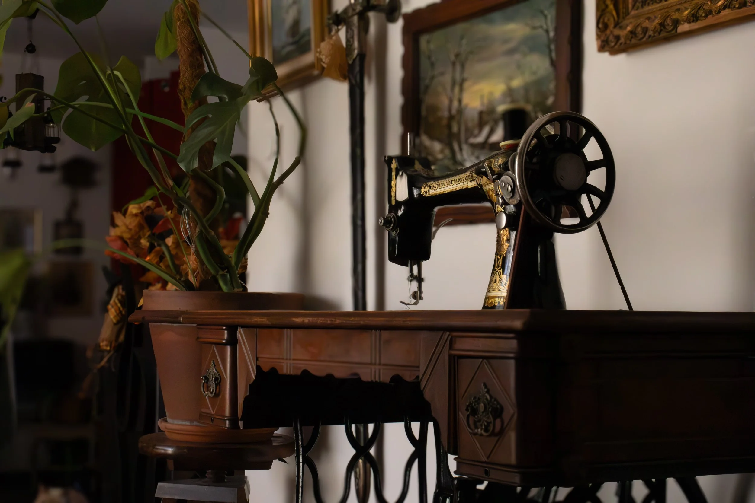 Une vieille machine à coudre noire avec des détails dorés, placée sur un meuble en bois.