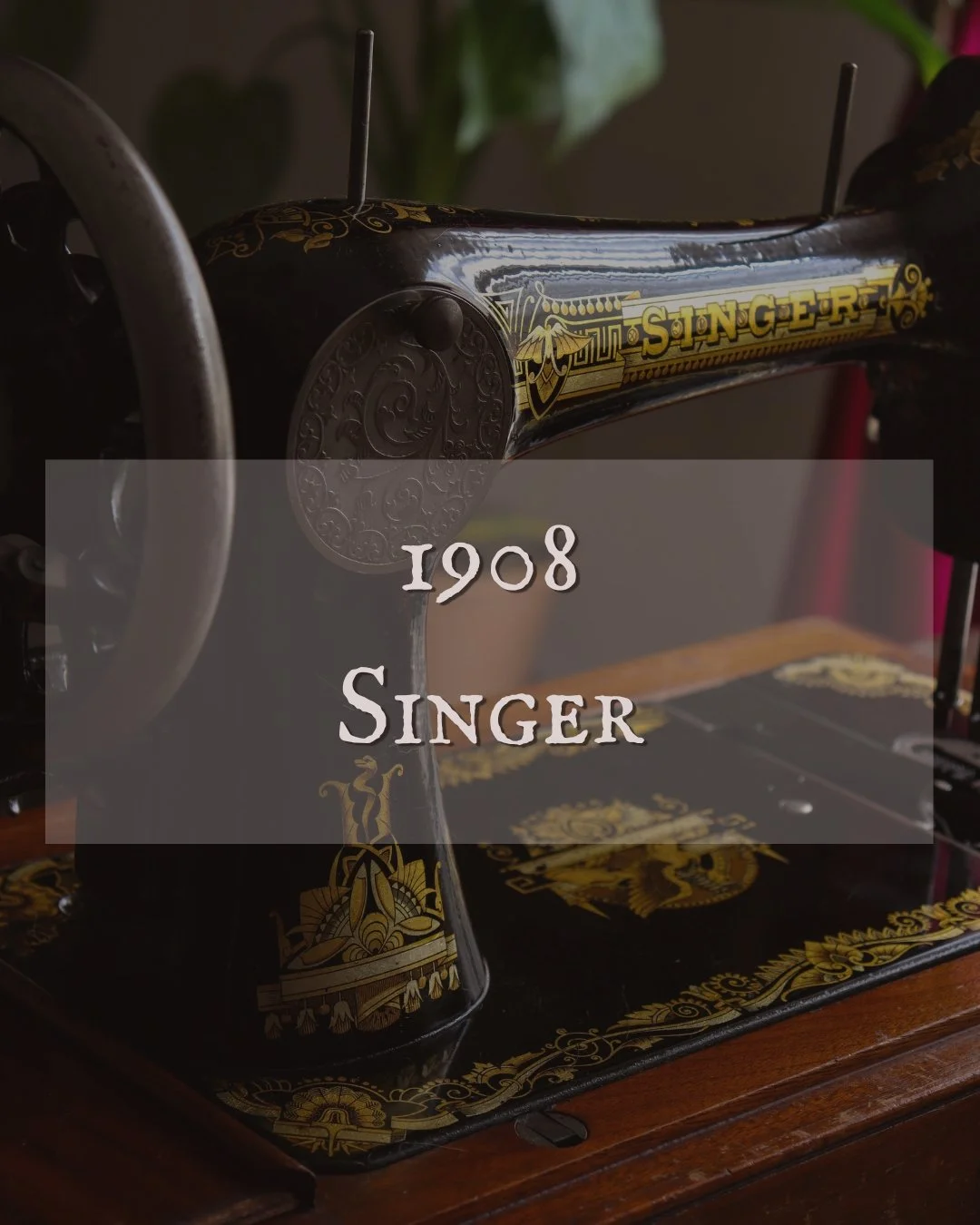 Une machine à coudre Singer vintage noire avec des décorations dorées, datant de 1908, posée sur une table en bois.