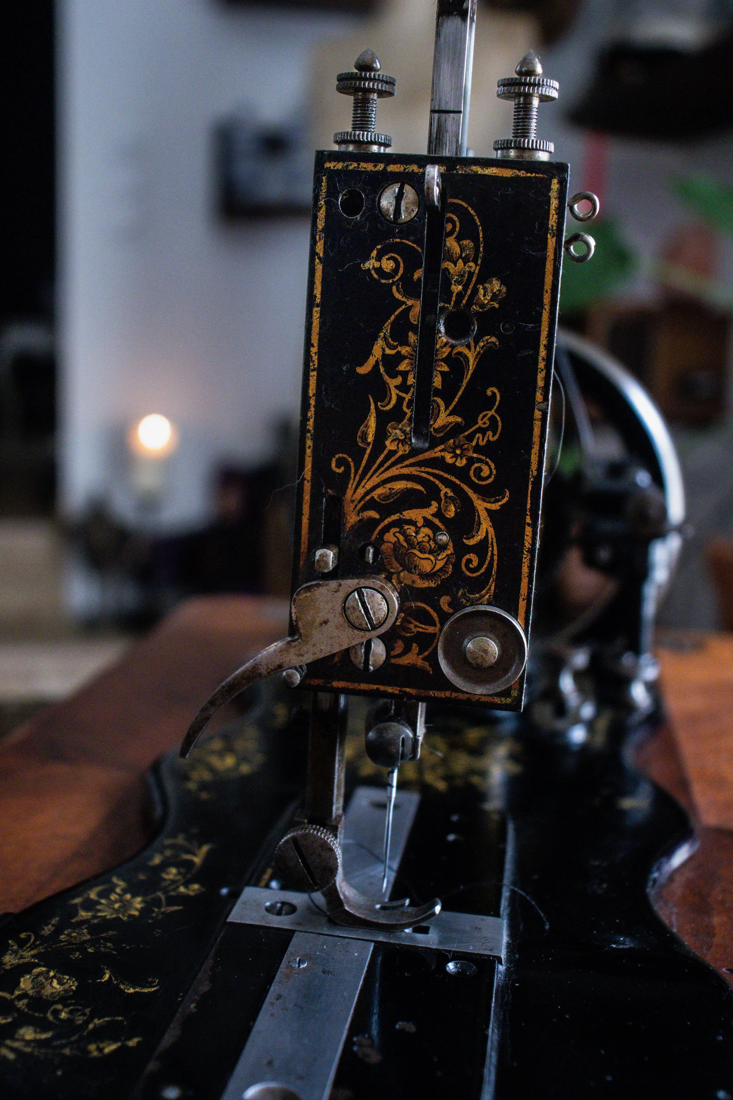 Machine à coudre ancienne noire avec des motifs dorés, vue centrale, avec pièces métalliques visibles, en intérieur.
