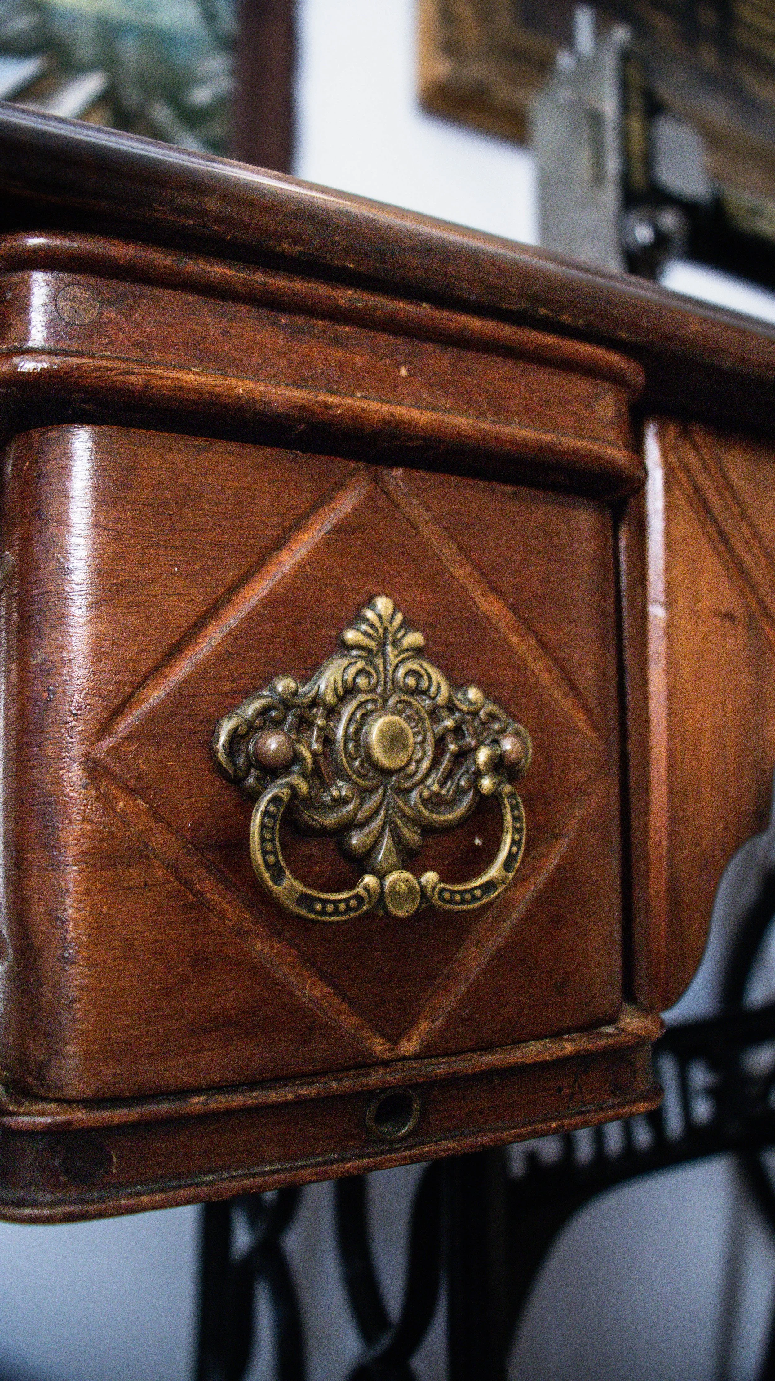Une boîte en bois avec un bouton en métal doré ornée d'un motif décoratif. La boîte est en bois brun foncé avec un aspect poli et vintage.