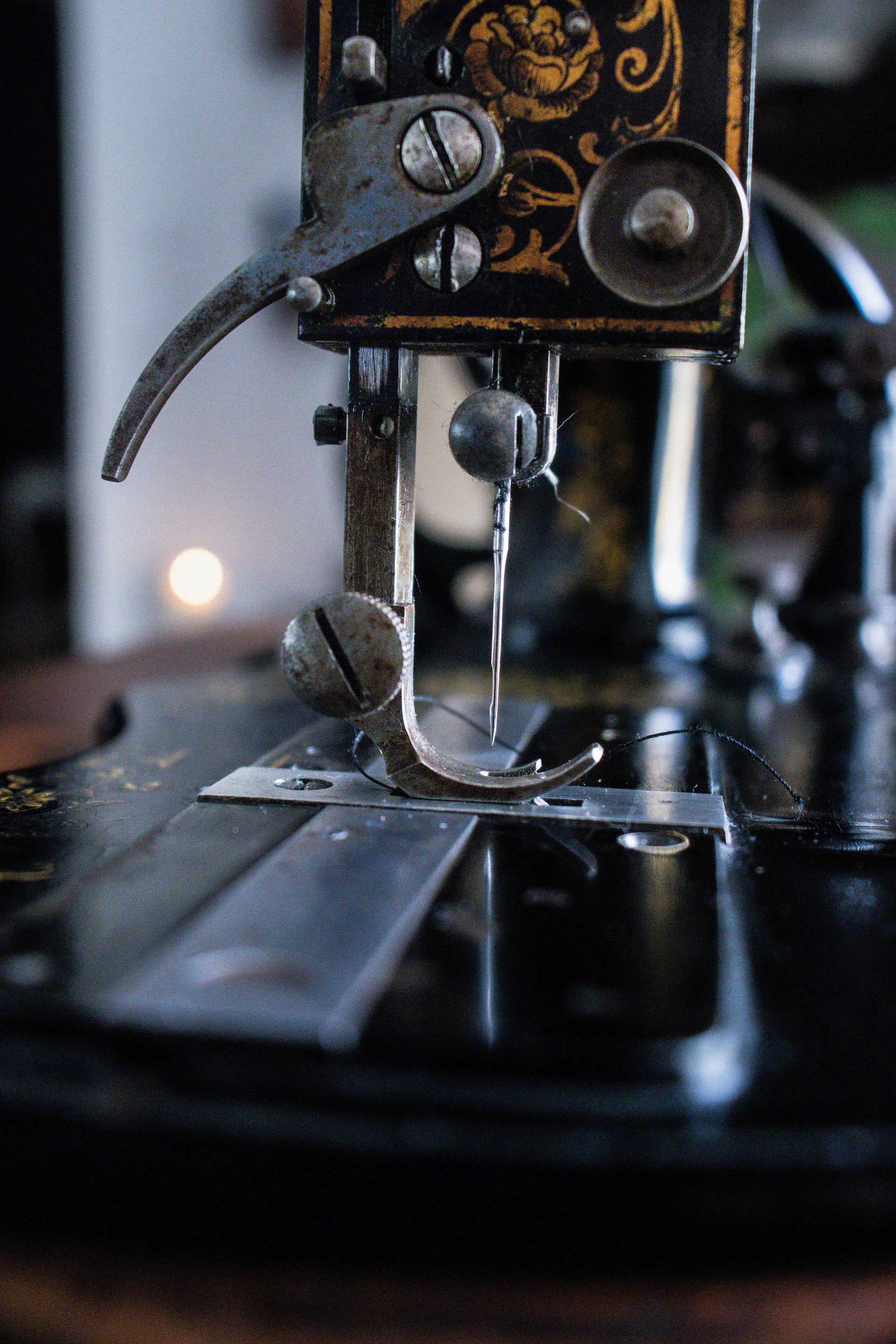 Une machine à coudre ancienne avec des composants métalliques, des vis et un tissu en dessous, dans un environnement de couture ou de réparation textile.