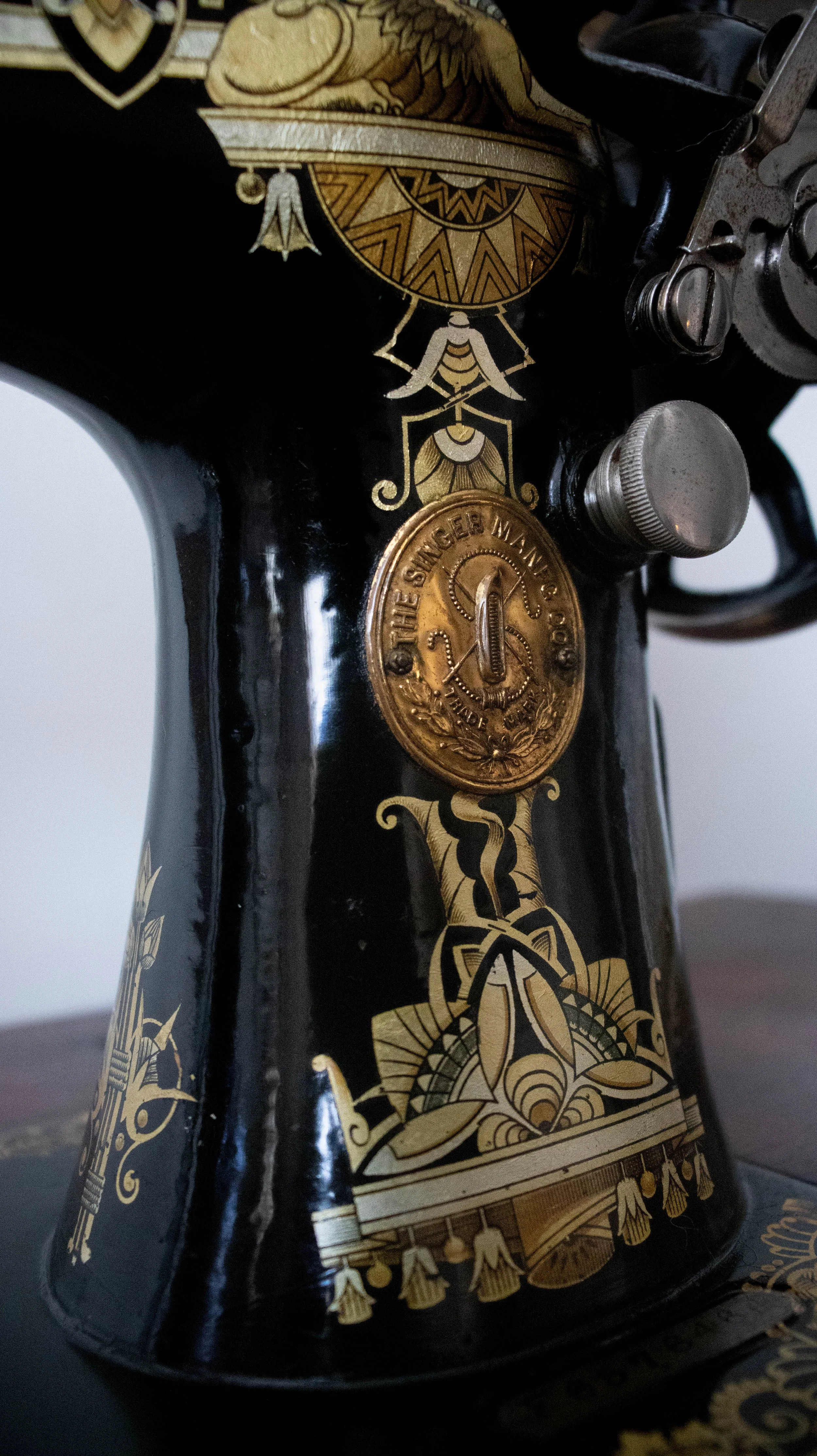 Partie avant d'une machine à coudre ancienne noire avec des décorations dorées et une plaque de marque 'The Singer Mfg Co'.