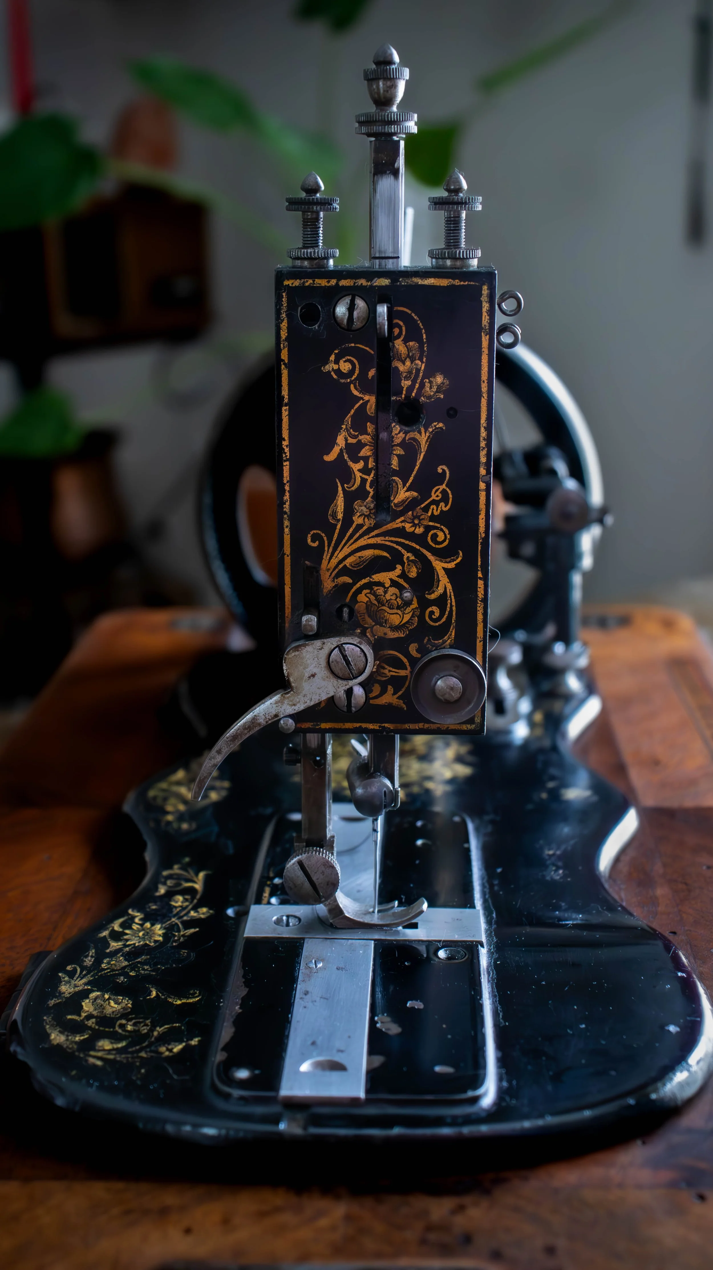 Machine à coudre ancienne avec décor floral noir et or, en cours de couture sur une table en bois.