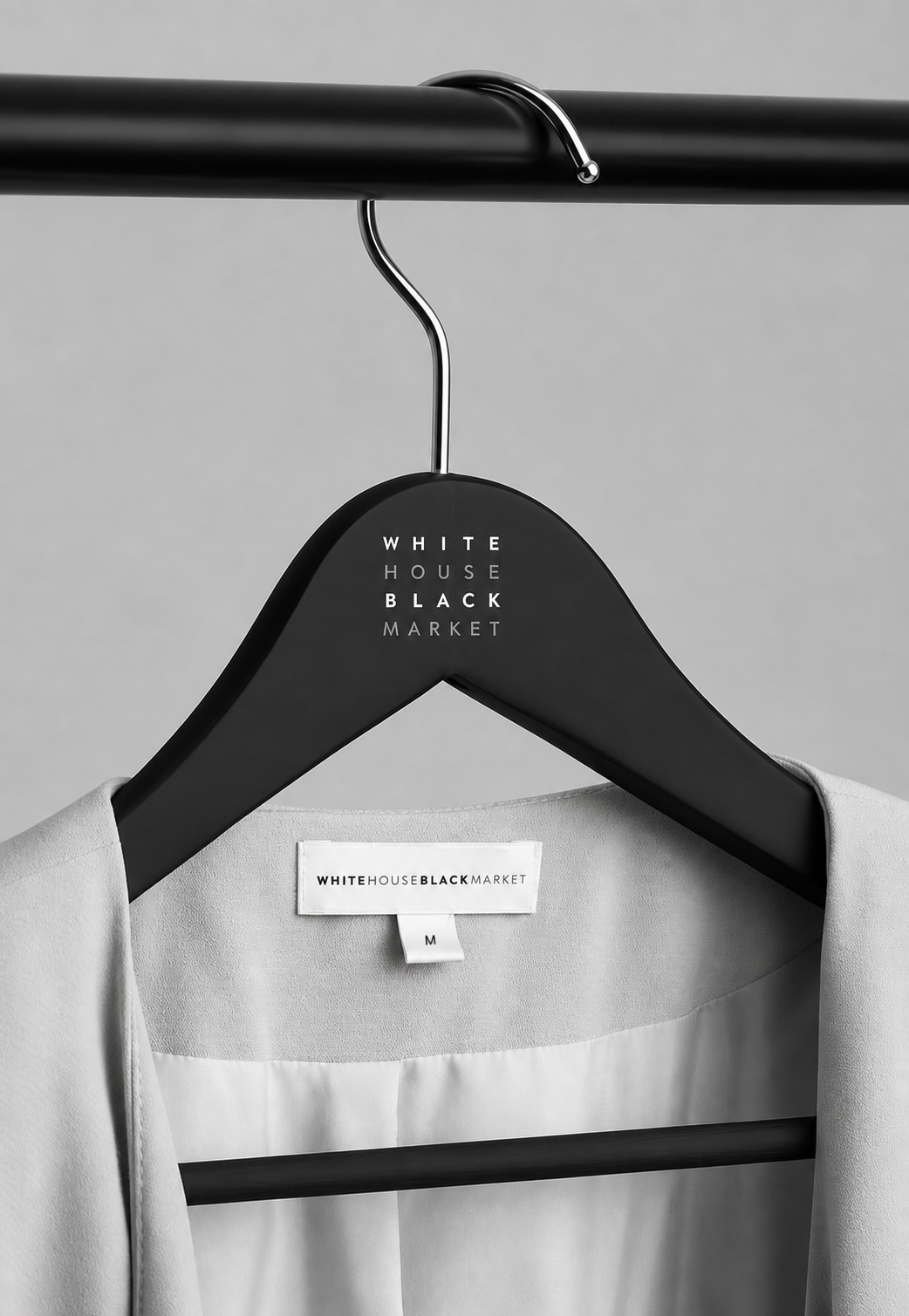 A black hanger with the words "WHITE HOUSE BLACK MARKET" printed on it in white, hanging on a black clothing rack, with a white garment partially visible below.