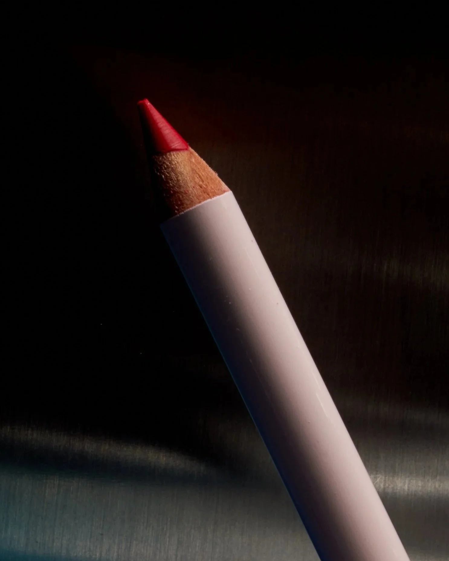 Close-up of a red pencil with a white body against a dark background.