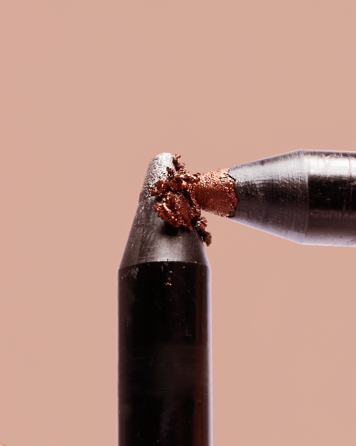 Close-up of a pipette dispensing a small amount of melted chocolate onto the tip of a tool, with a plain light-colored background.