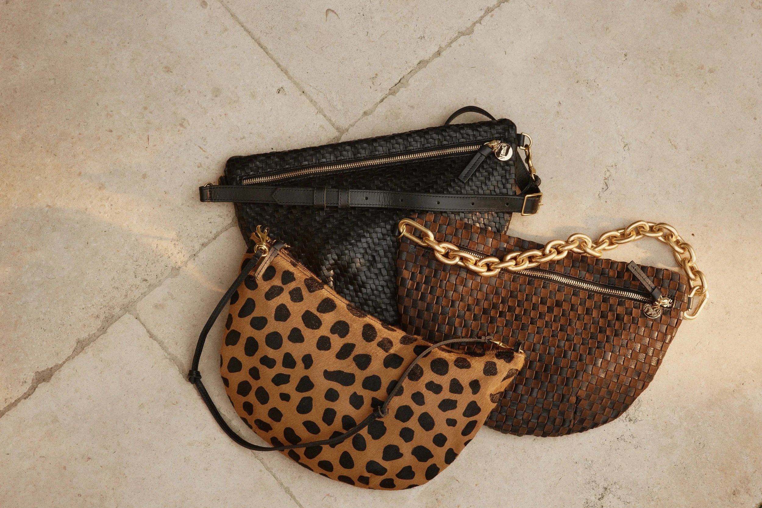 Four handbags placed on a tiled floor. The handbags feature various patterns, including animal print and woven-texture designs, with some having gold chains and zippers.