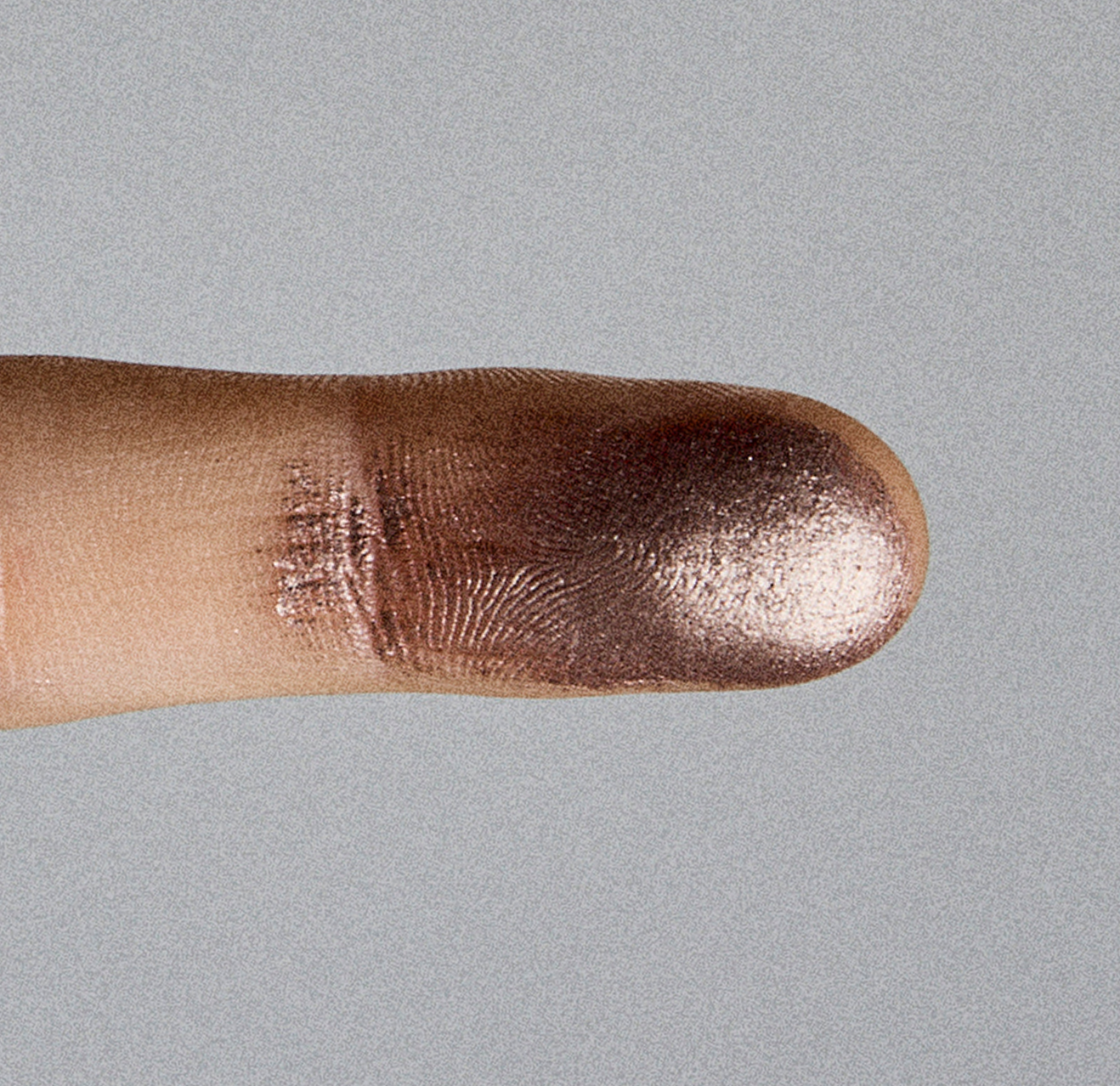 Close-up of a finger with shiny metallic pink nail polish on a gray background.