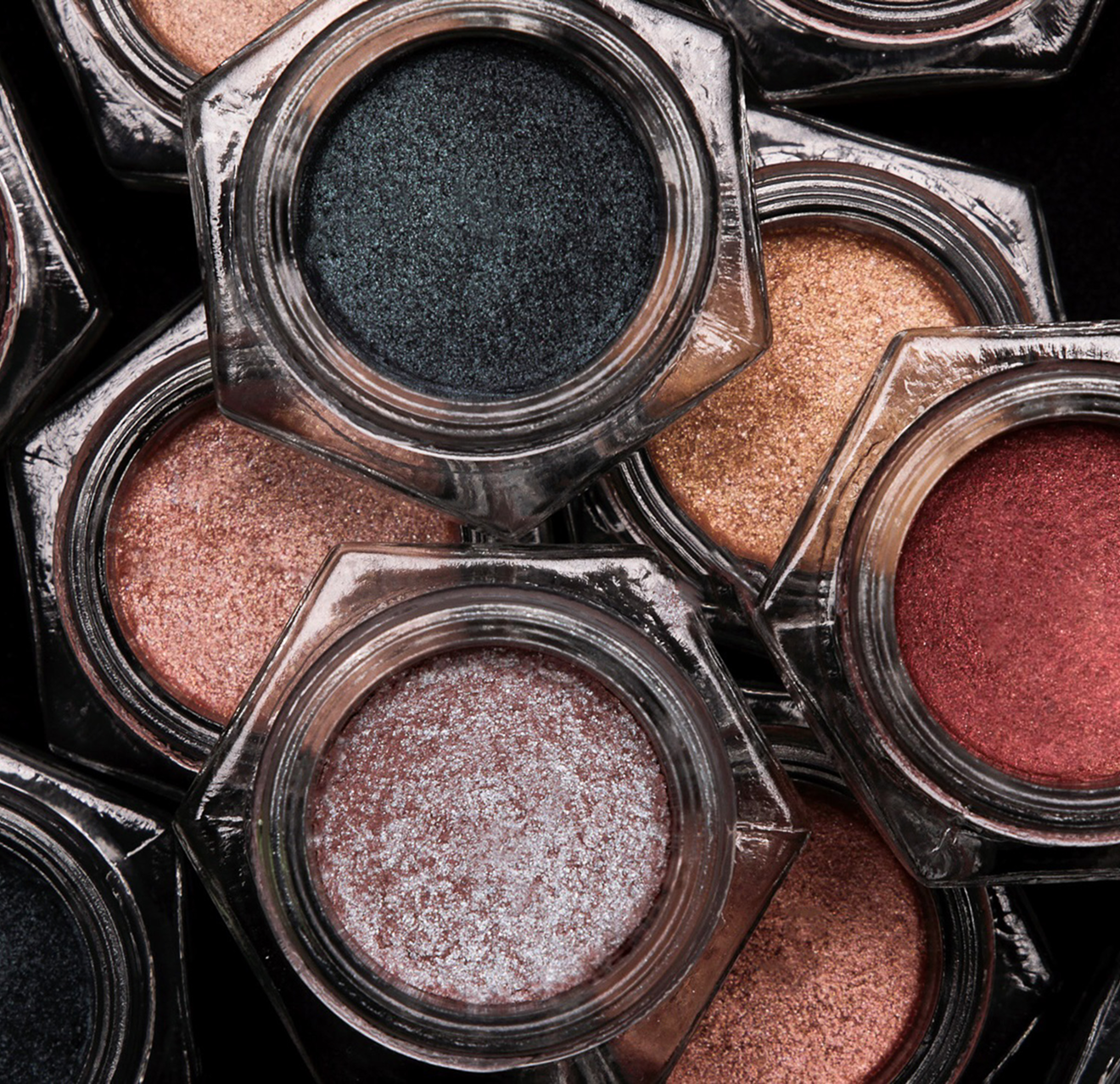 Close-up of multiple open jars of glitter eyeshadows in various shades including black, pink, gold, and red.