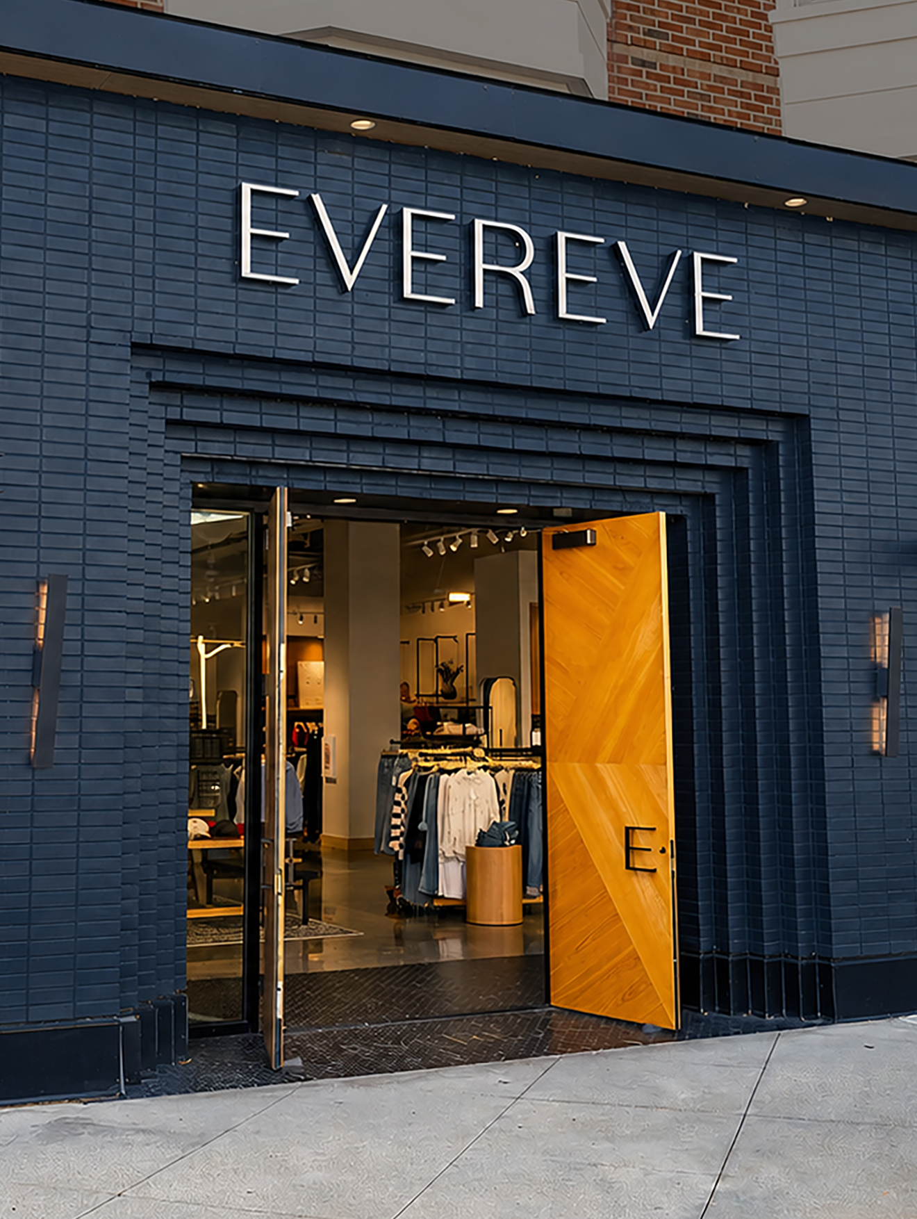 Store entrance with blue brick facade, large open door, and clothing displays inside.