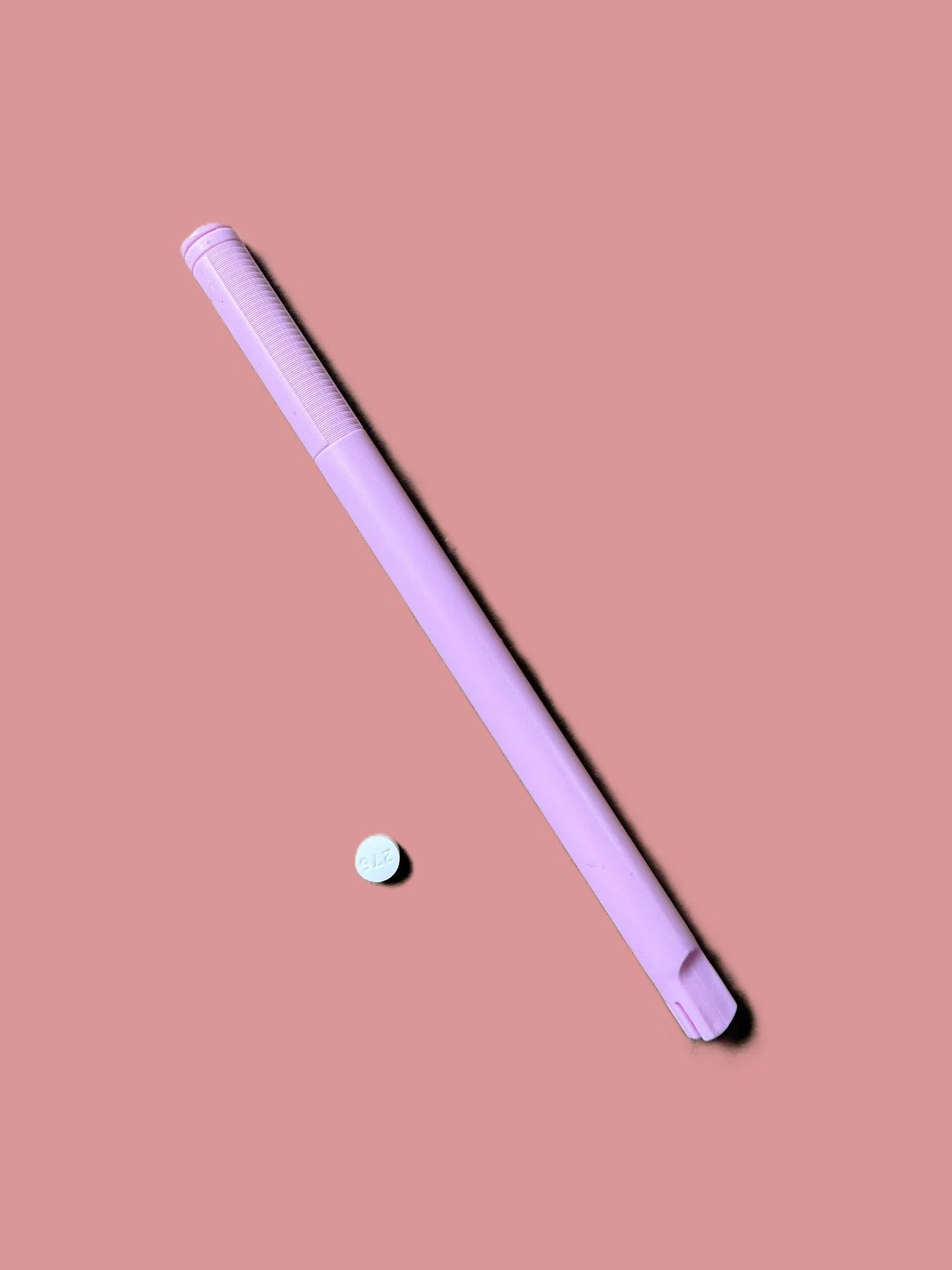 A pink pen and a white pill with the letters 'ELZ' printed on it, placed on a pink background.
