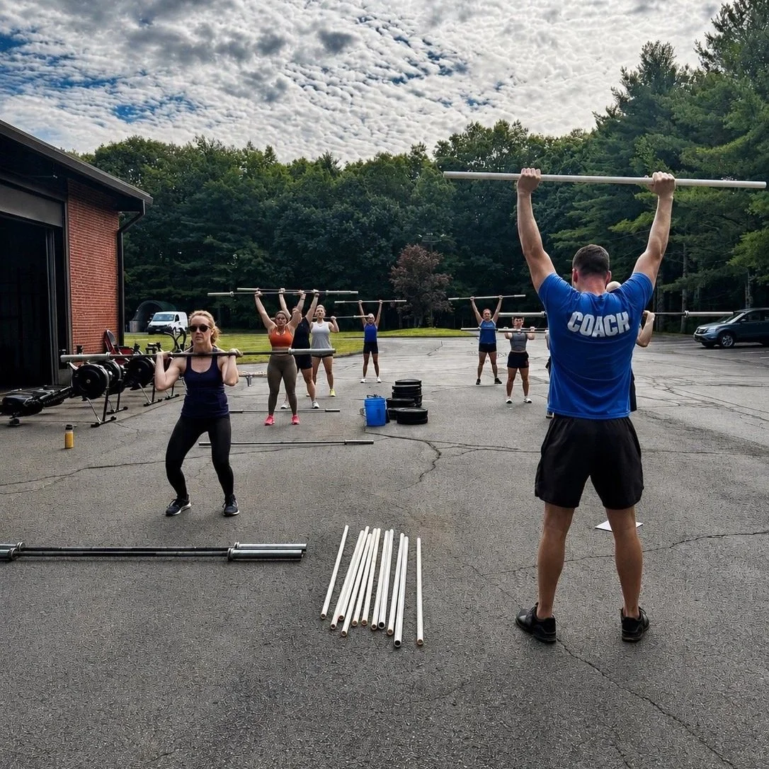 Outdoor group fitness class at Override North in Avon, CT with members lifting barbells during a coached workout.