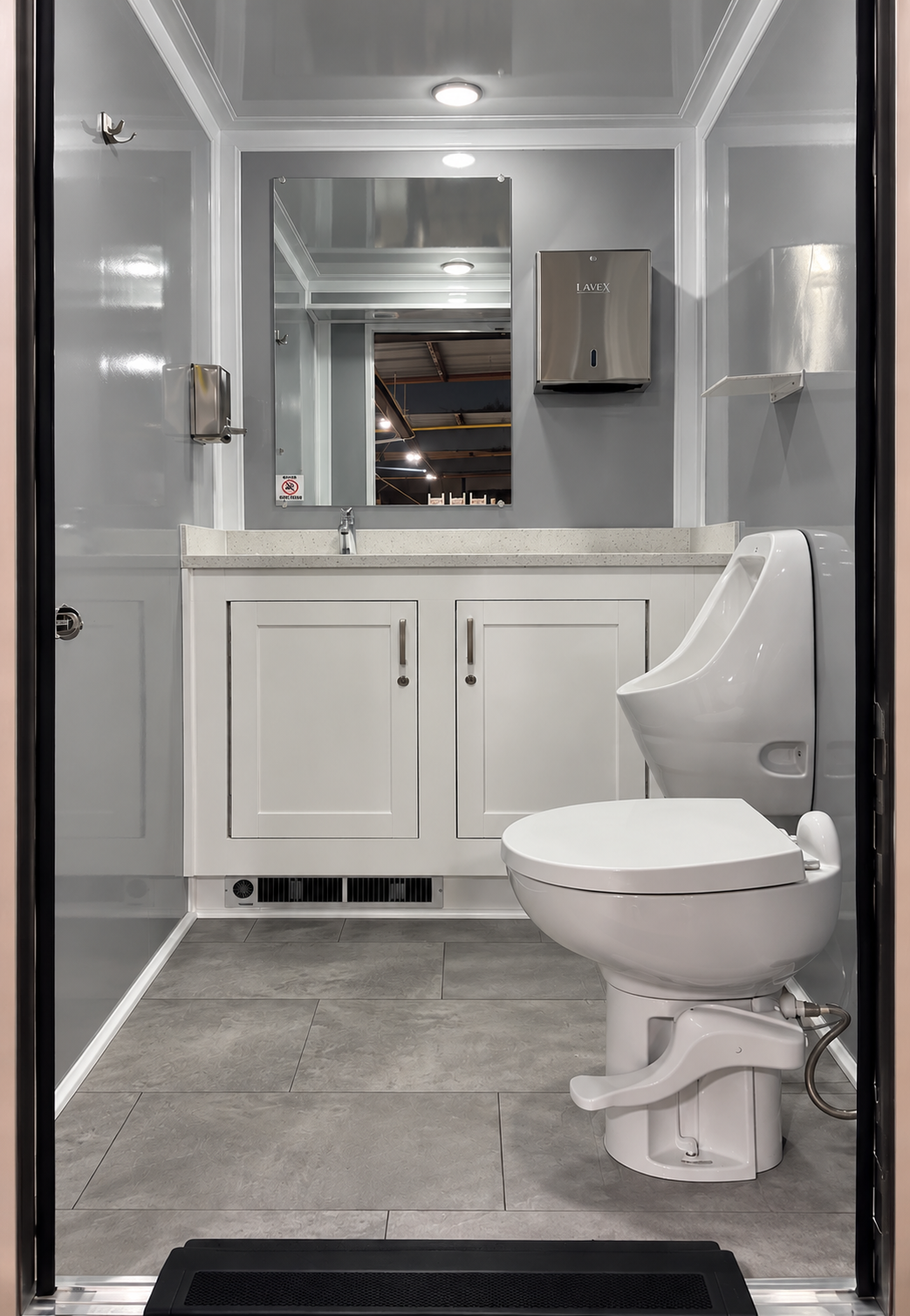 A clean, modern restroom with a white toilet, white cabinet with doors, a sink with a mirror above, a stainless steel soap dispenser, a paper towel dispenser, and a no smoking sign.