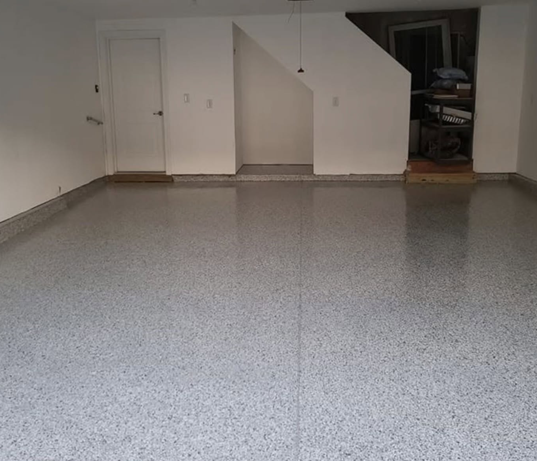Empty room with speckled gray epoxy floor, white walls, a white door, and a small storage area with shelves in a corner.