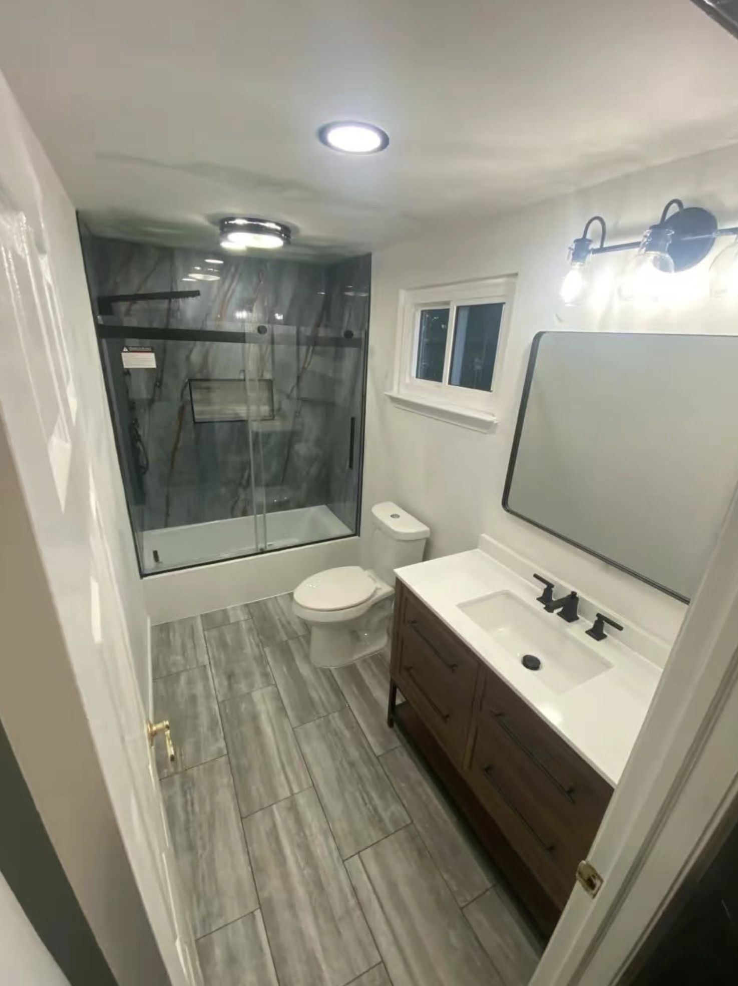 Bathroom with a shower enclosure, toilet, vanity with sink and mirror, window, and tiled floor.
