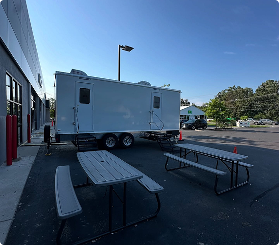 Mobile food trailer with entry stairs in a parking lot near a building, with picnic tables and orange traffic cones.