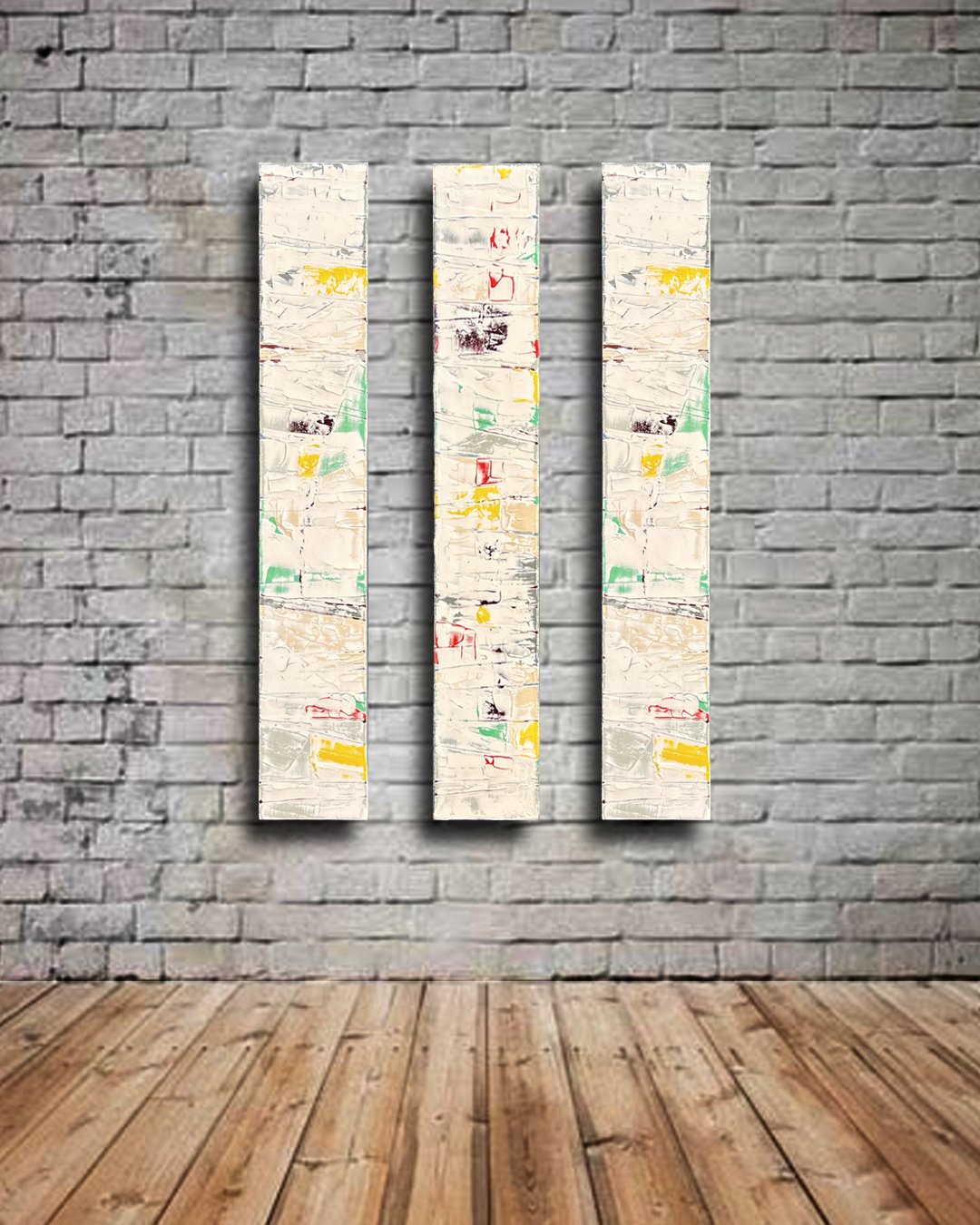 Three vertical abstract paintings with a textured surface, featuring patches of yellow, green, red, and black on a white background, mounted on a brick wall in an art gallery.