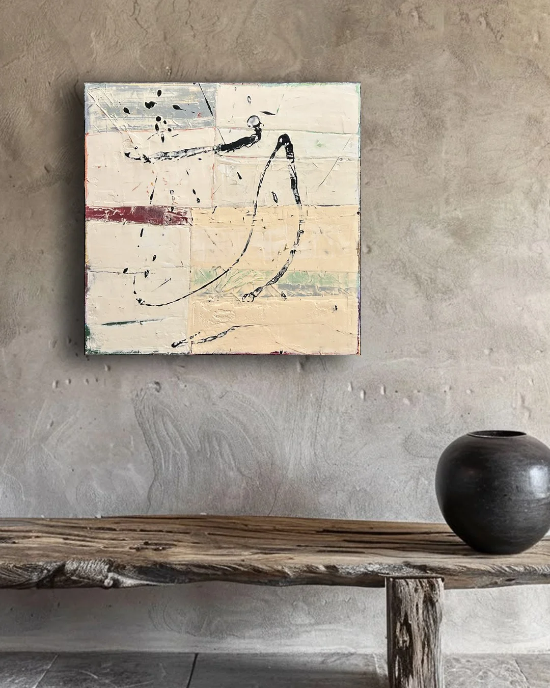 Abstract painting with black lines and splatters on a textured wooden panel wall, above a rough wooden shelf with a black ceramic vase.