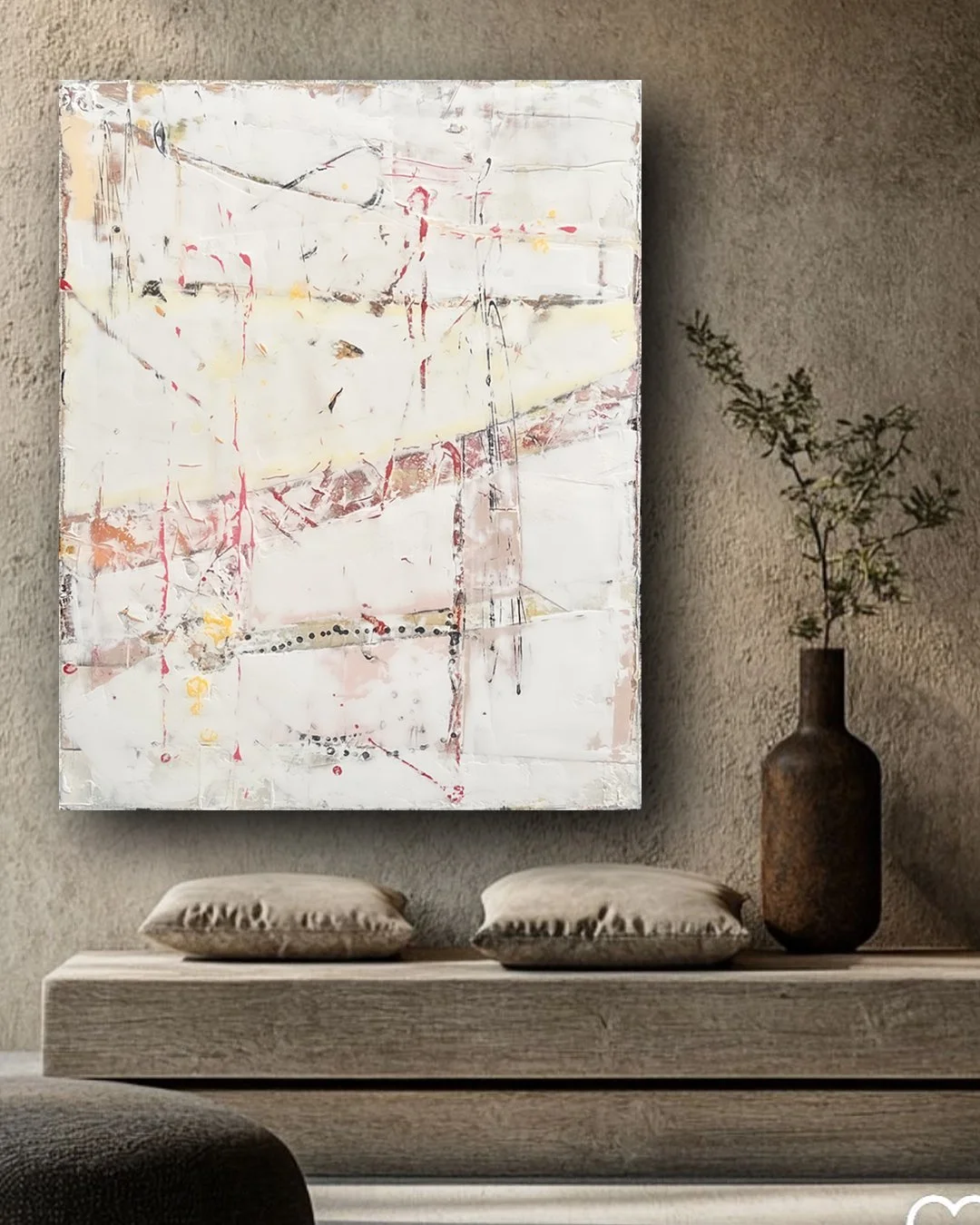 Decorative abstract painting with mostly white and light colors hanging on a textured wall, with two beige cushions on a wooden console below and a tall brown vase with a green plant on the right side.
