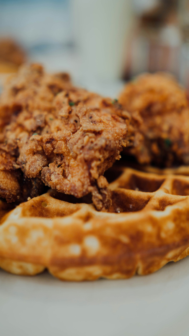 Close-up of crispy fried chicken drumsticks on a plate with waffles.