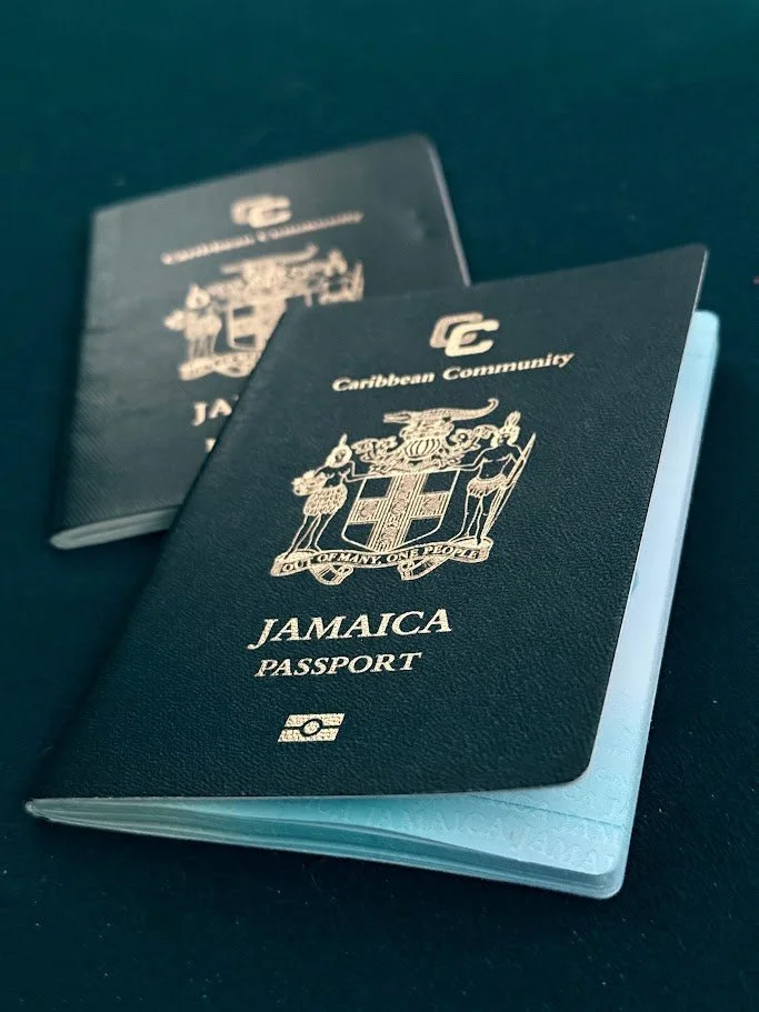 Close-up of two Jamaican passports with black covers and gold emblem, placed on a dark surface.