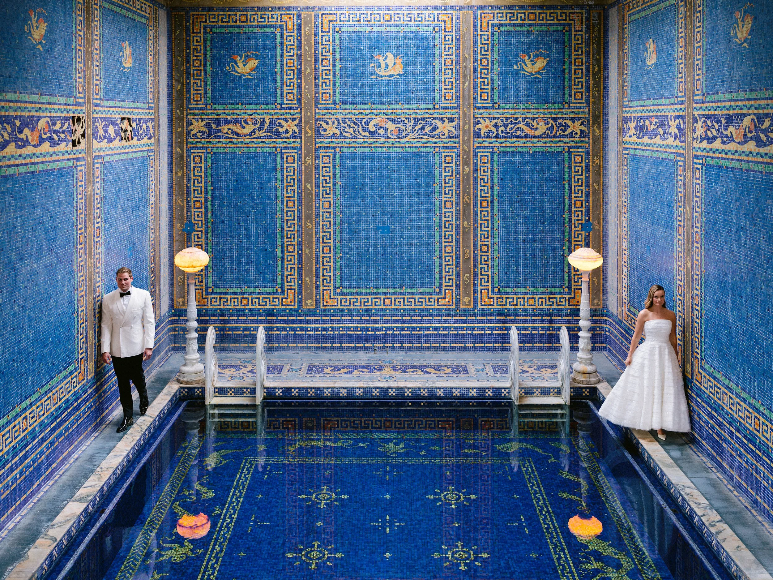Elegant indoor space with blue mosaic tile walls, a small pool or water feature, and two people dressed in formal attire standing near the water.