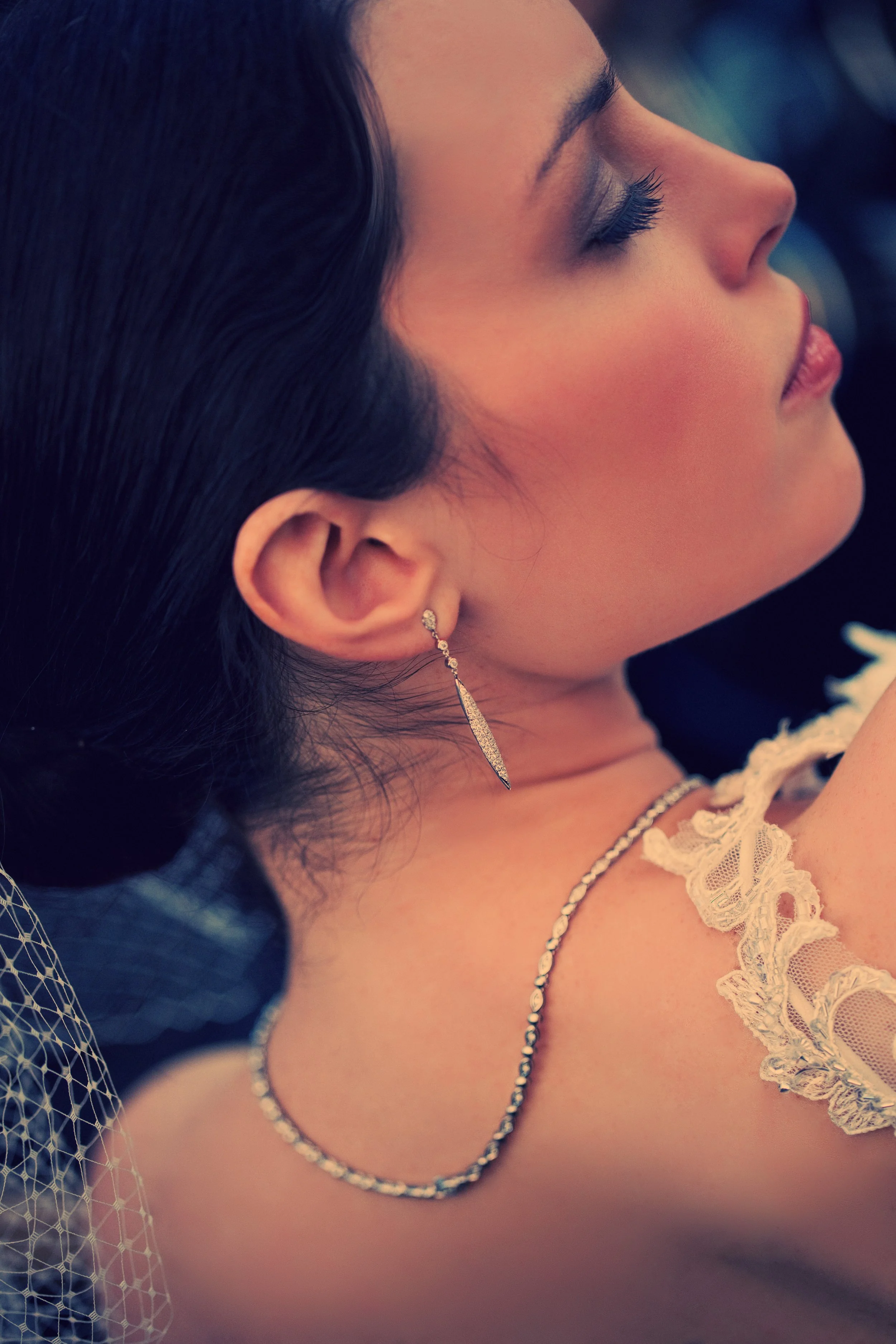 Close-up of a bride wearing a long pointed drop earring and a delicate necklace.