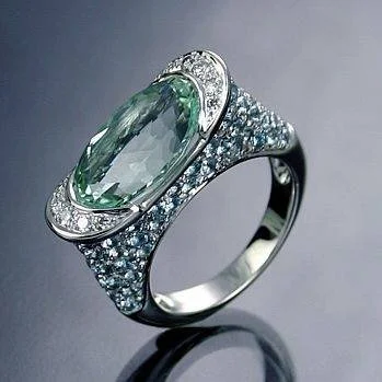 Large oval pale-green center stone with curved clear accents and small blue-green shoulder stones.