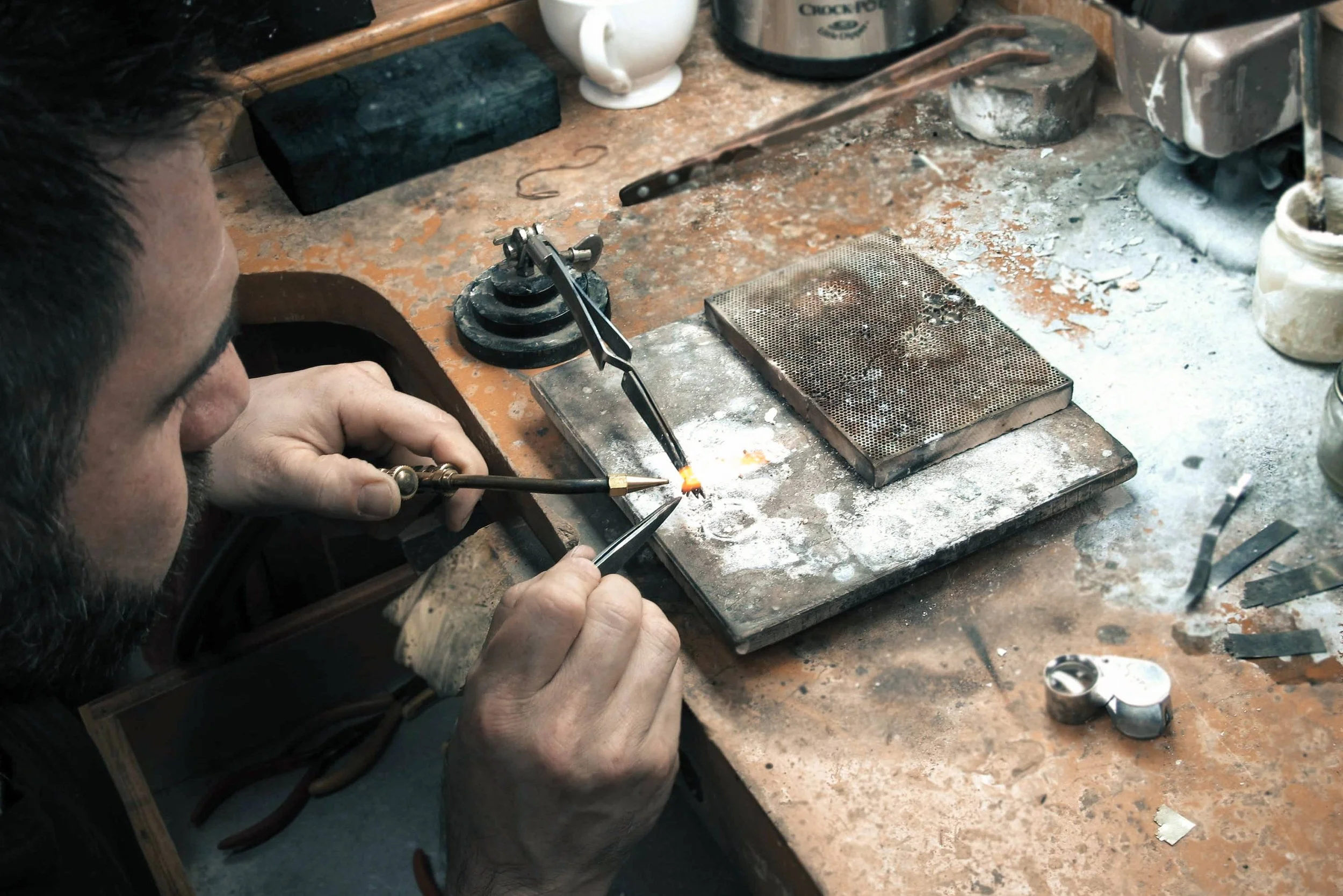 Serjeo applying a small torch flame to a jewelry component held over a soldering block.