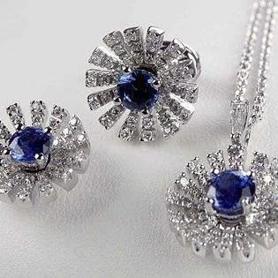 Pair of floral earrings and a matching pendant with dark-blue centers and radiating clear-stone petals.