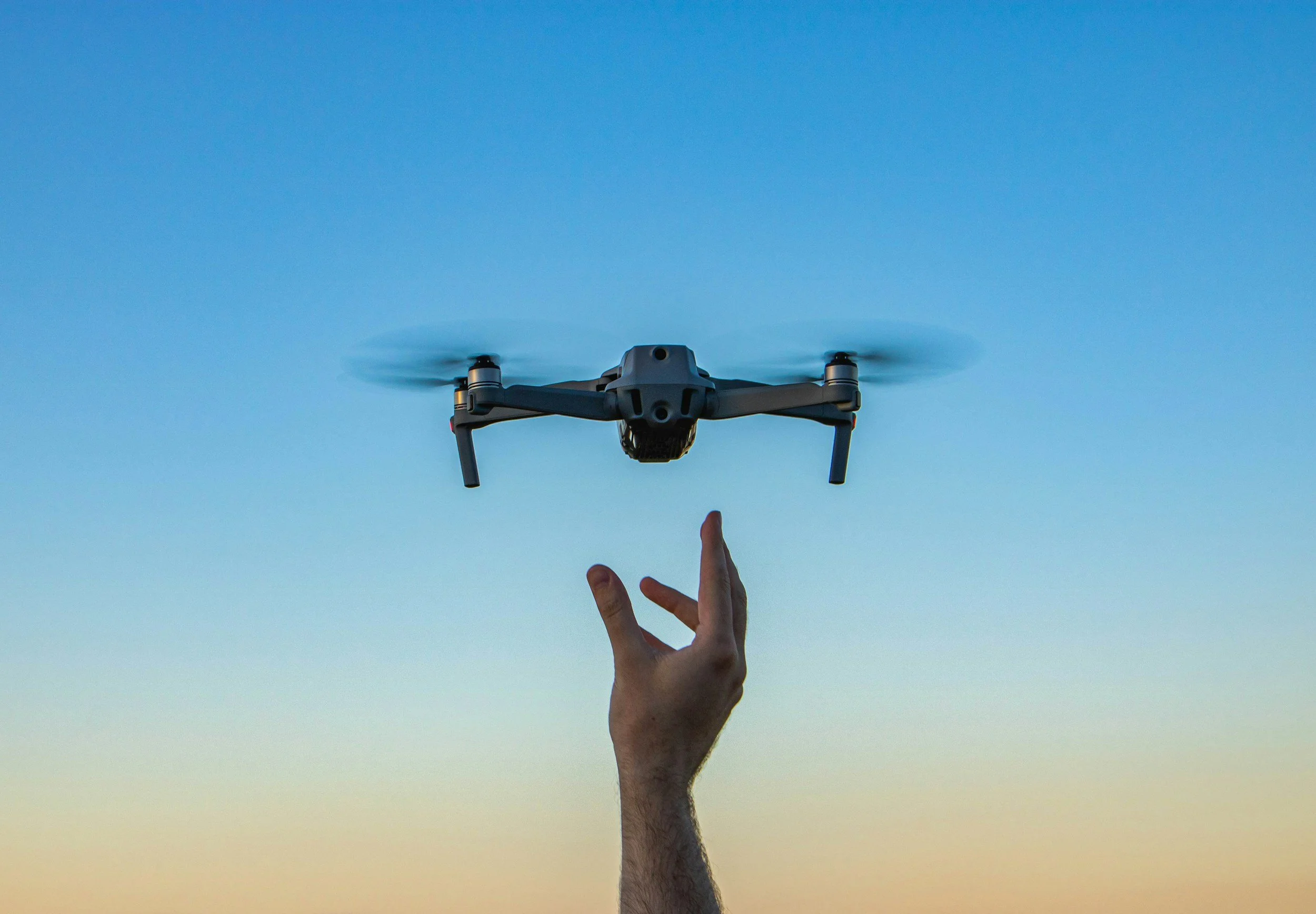 A person holding a drone with their fingers, with a clear blue sky in the background.