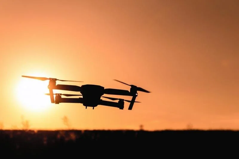 Silhouette of a drone flying at sunset with an orange sky in the background.