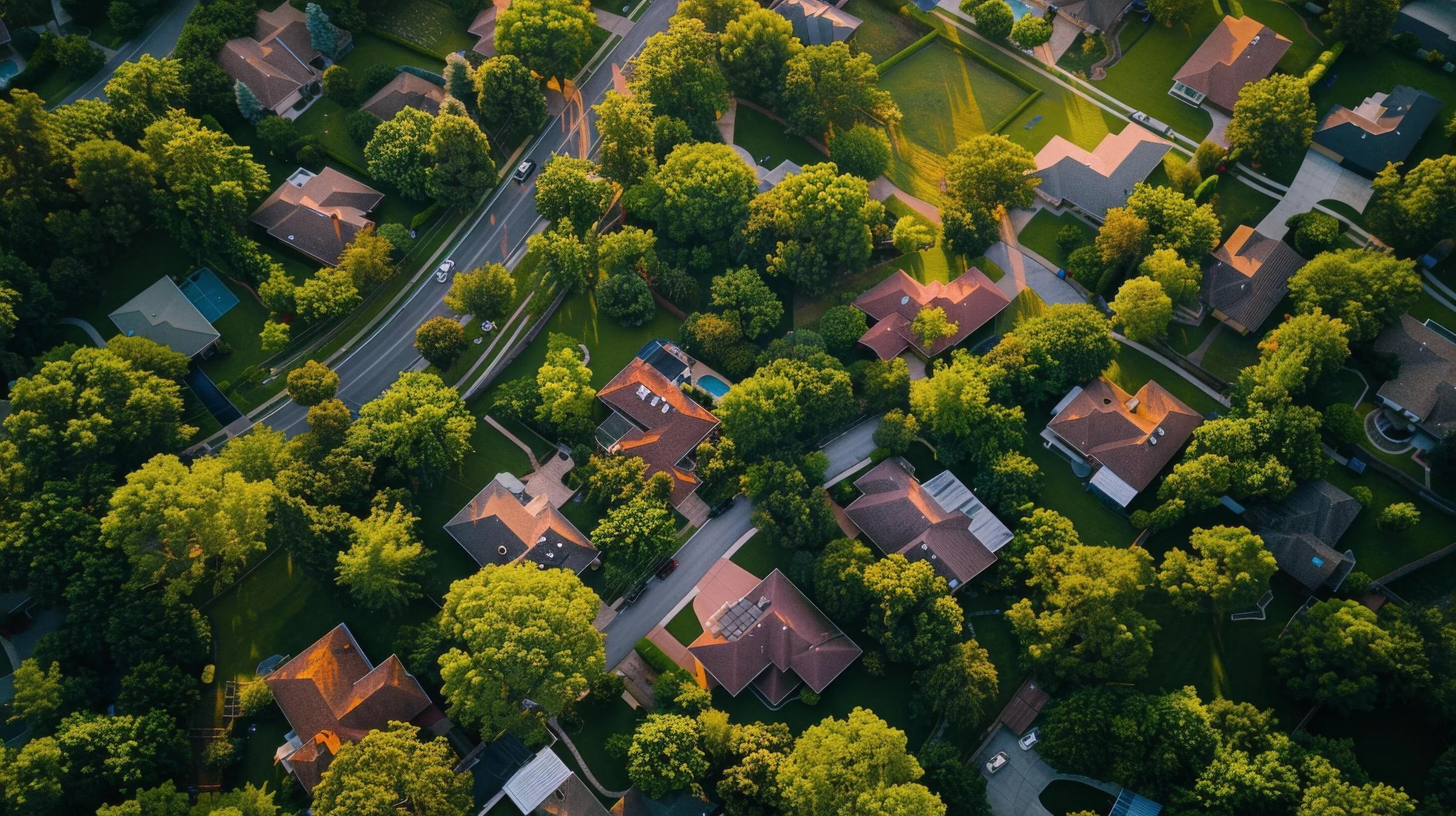 Aerial view of a suburban neighborhood with houses, green lawns, trees, and streets at sunset.