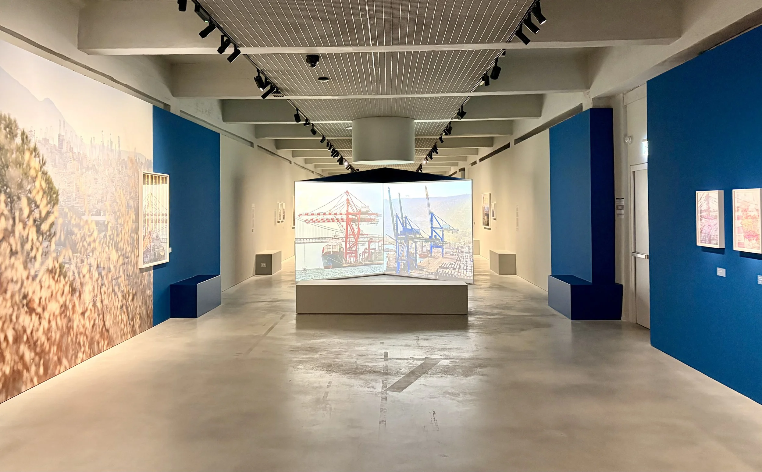 Modern maritime museum gallery with blue walls, port photography, framed artwork, and a large projection of shipping cranes and containers