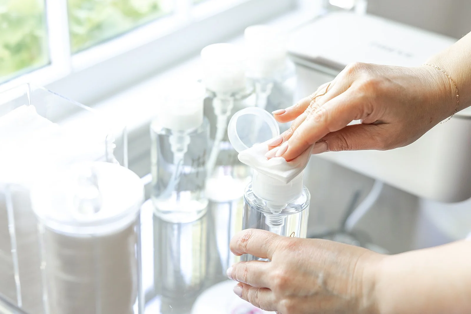 A person filling a skincare bottle with cream from a jar in a well-lit room.