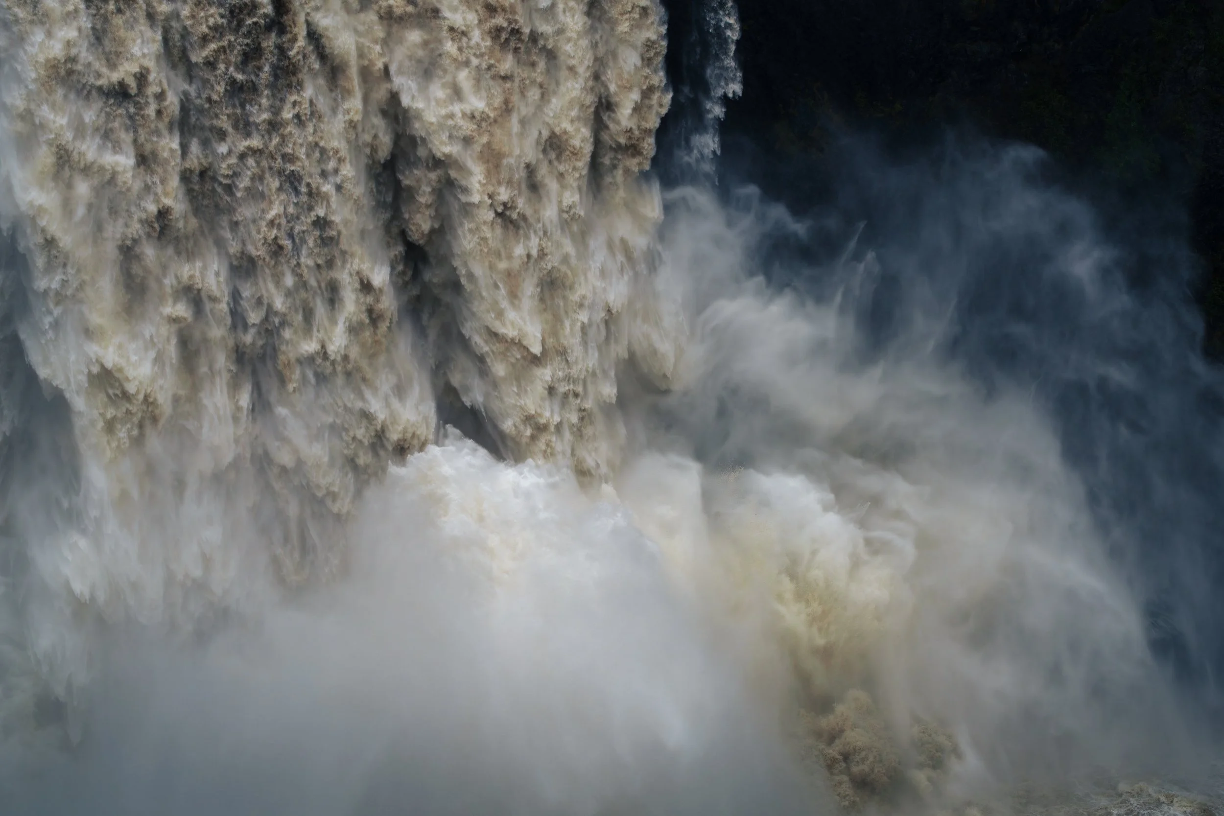Powerful turbulent water plunges over Snoqualmie Falls and explodes into mist and spray below.