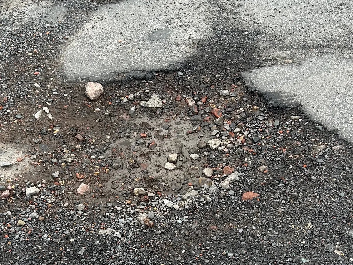 A section of damaged asphalt with a sunken pothole filled with loose gravel and dirt.