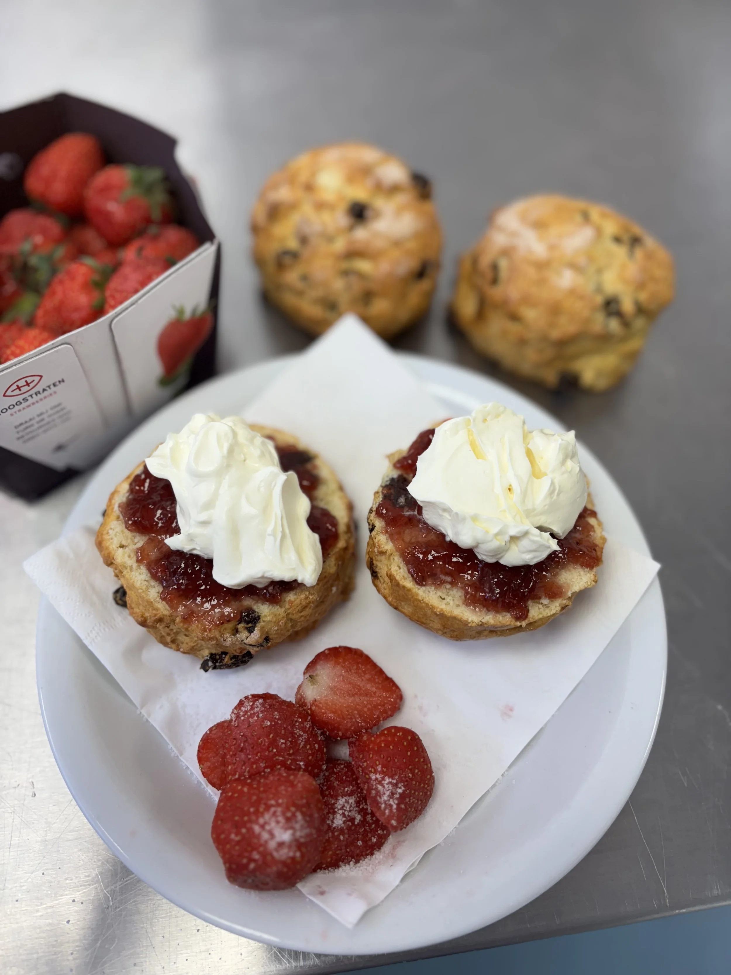 Plate with two strawberry cupcakes topped with whipped cream and a side of fresh strawberries, with two chocolate chip muffins in the background.