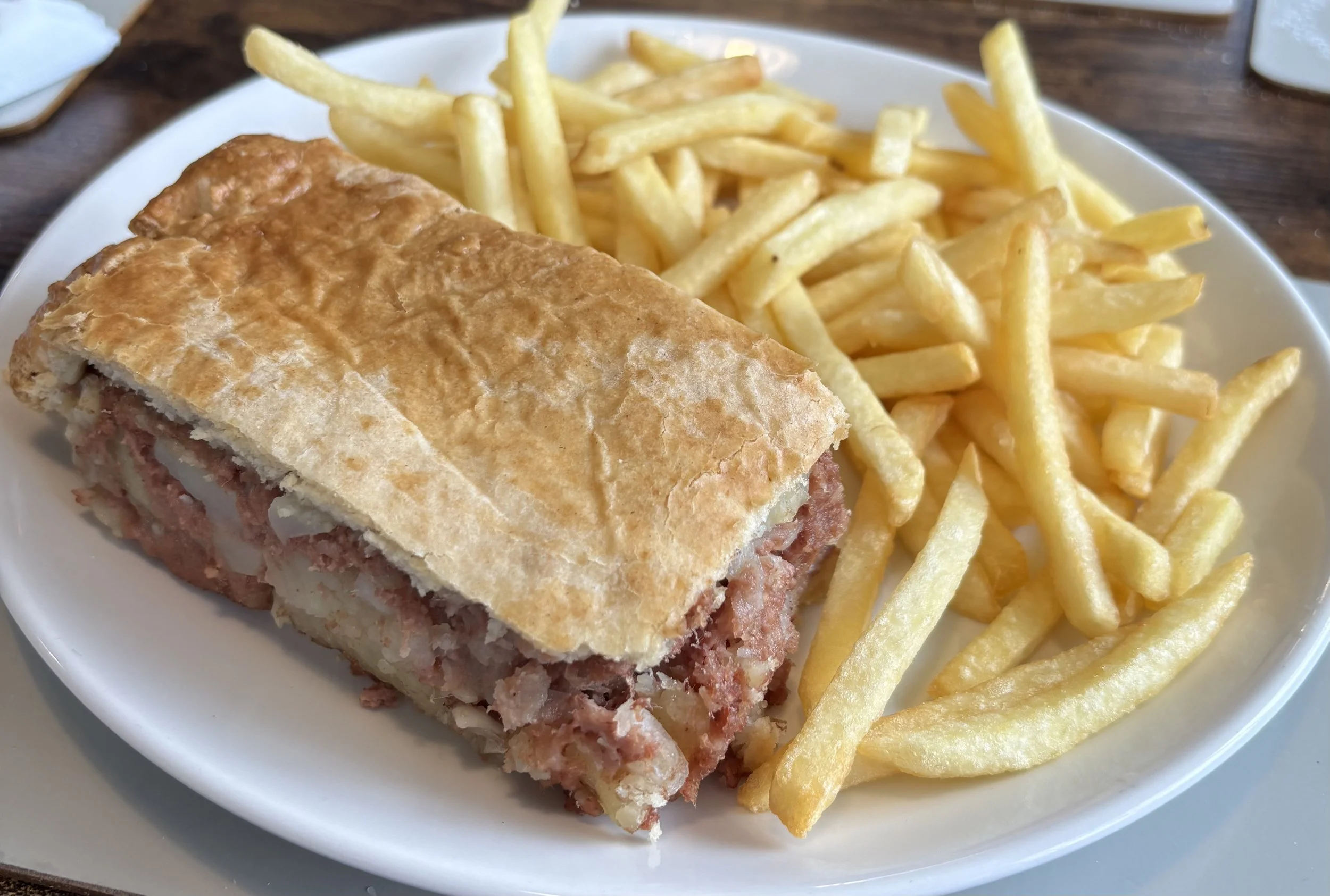 A white plate with French fries and a savory meat pie with a flaky crust.